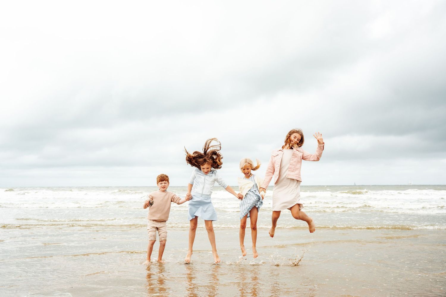Four people jumping joyfully together on a cloudy beach.