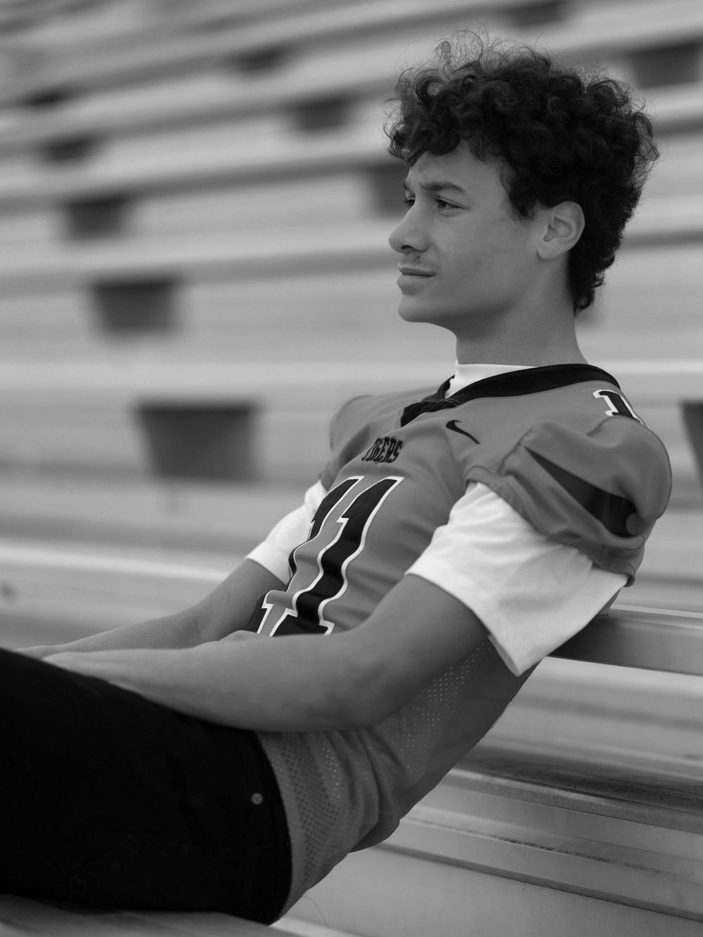 Black and white photo of athlete stretching on bleachers during training.