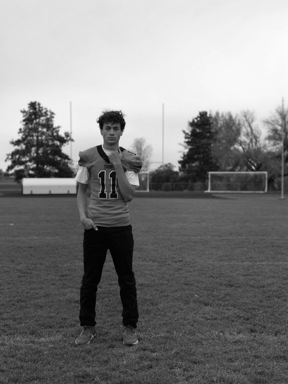 A black and white photo of an athlete wearing jersey number 11 standing on a soccer field with a goal in the background.
