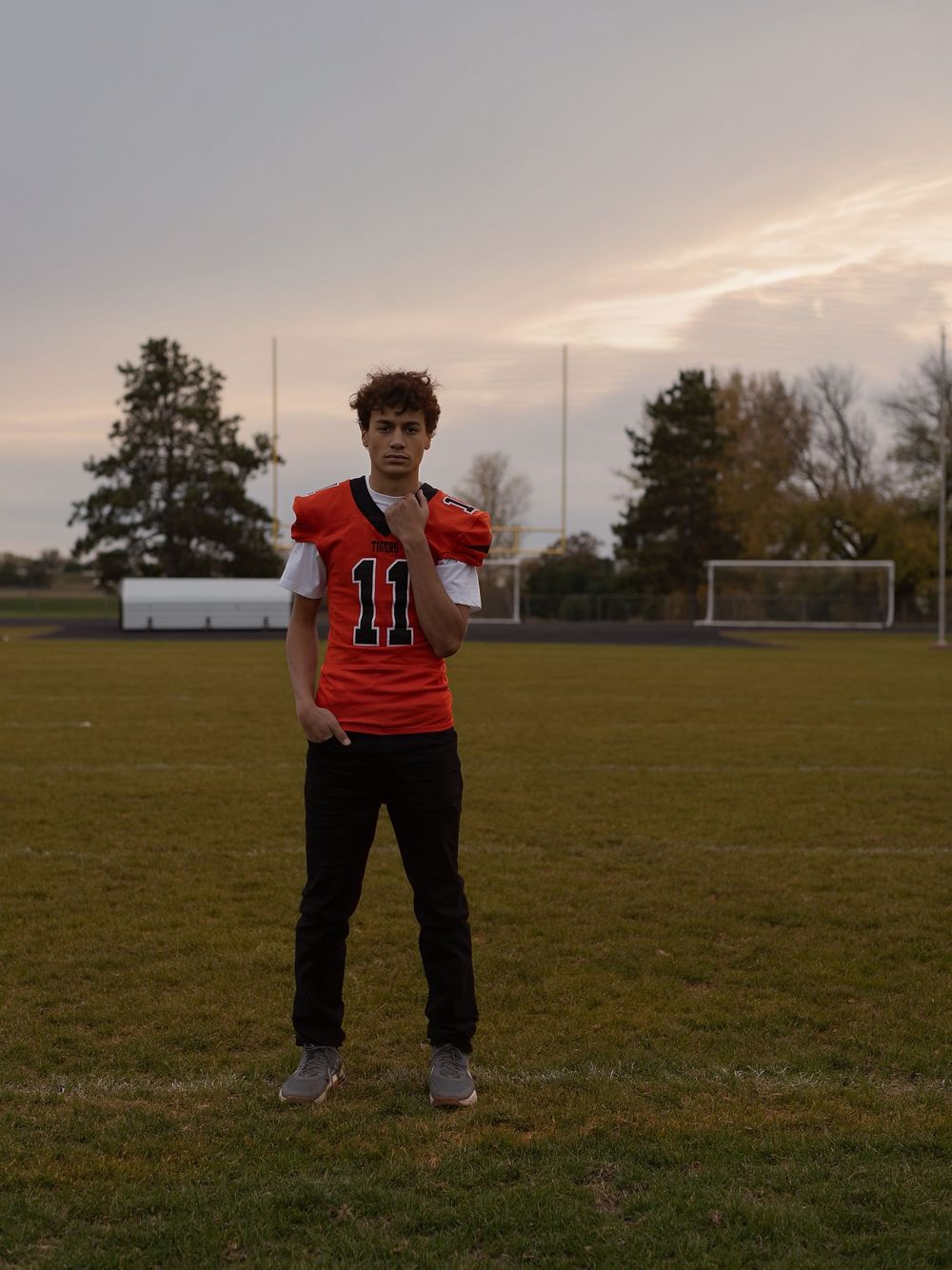 Football player in red jersey stands on grassy field at sunset during practice session.
