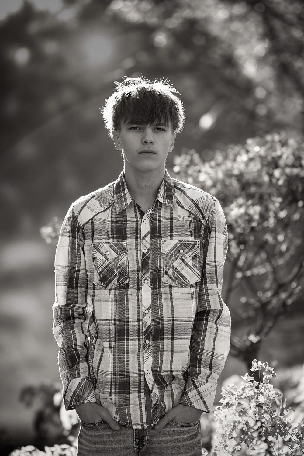 Black and white portrait series showing someone in a plaid shirt surrounded by flowering spring blossoms in nature.