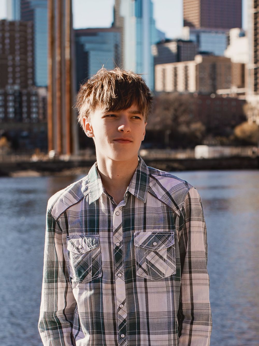 Portrait series showing someone wearing a plaid button-up shirt against an urban waterfront backdrop.