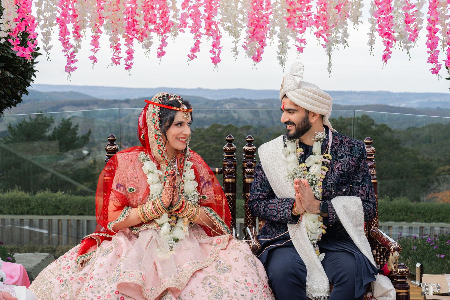 A couple dances during a wedding celebration in front of an elegant white backdrop with floral decorations and string lights.