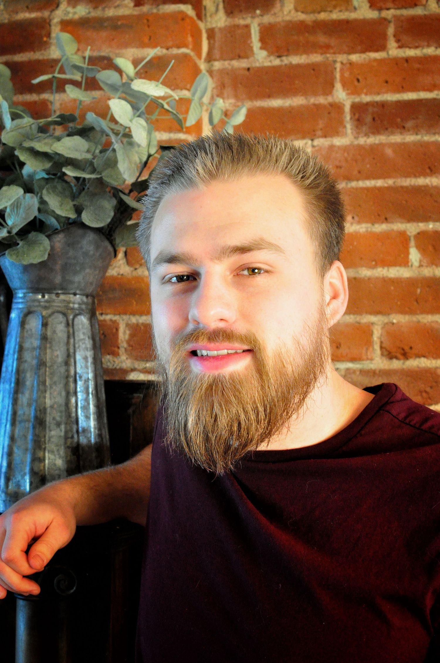 Young man with a beard poses in front of a brick wall