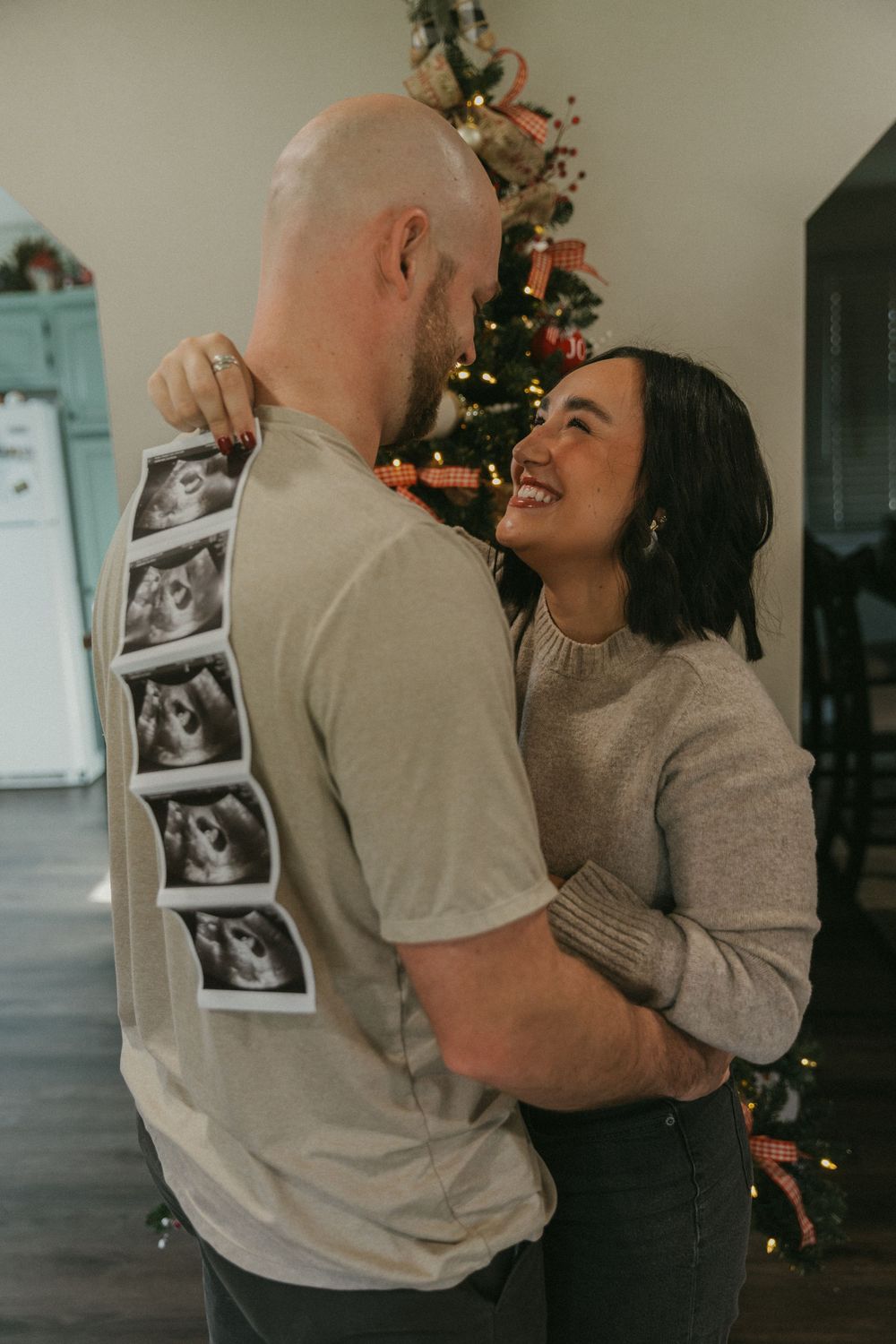 Couple shares intimate moment while displaying ultrasound photos on shirt during pregnancy announcement.