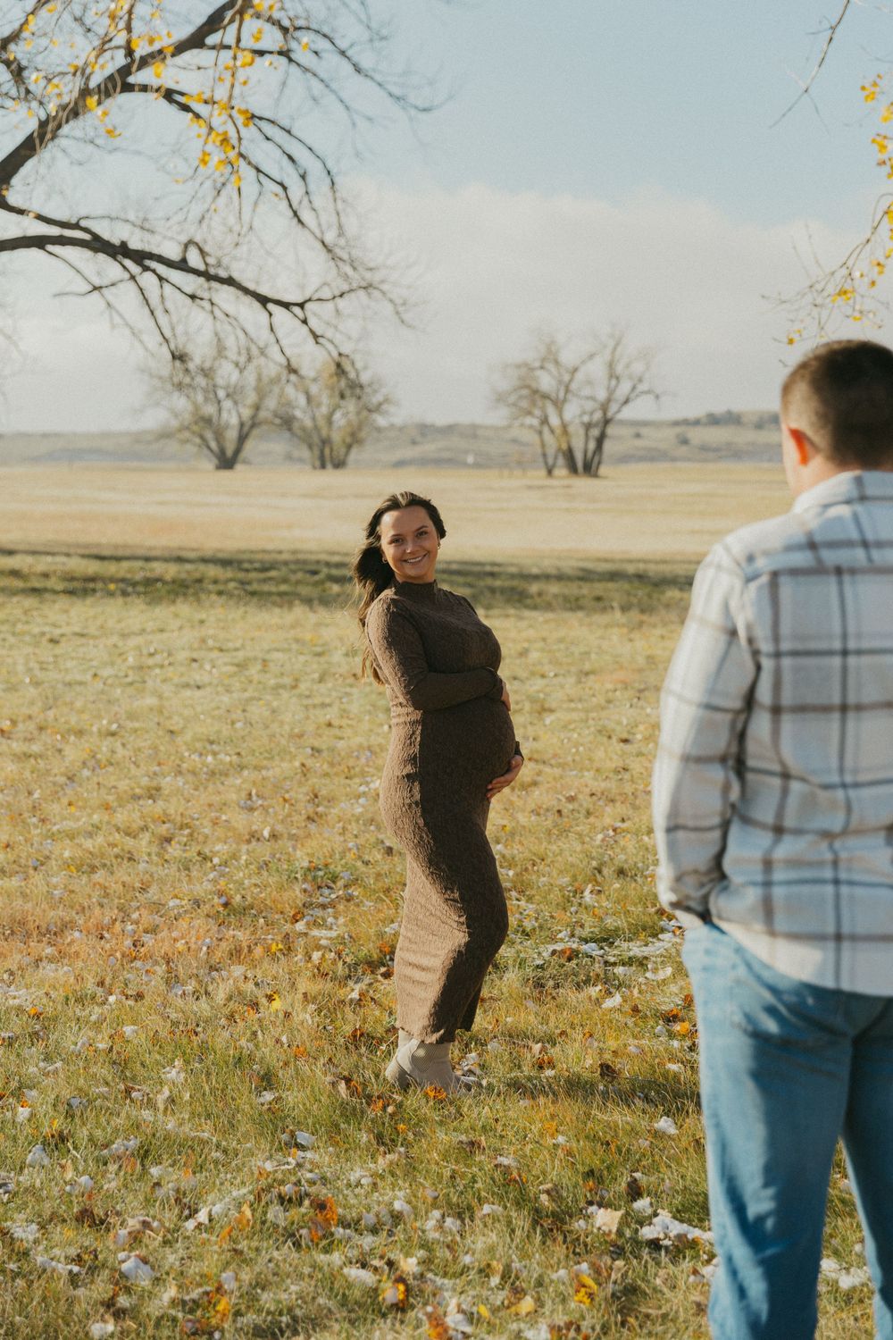 Expectant couple poses in open field during golden hour maternity photoshoot.