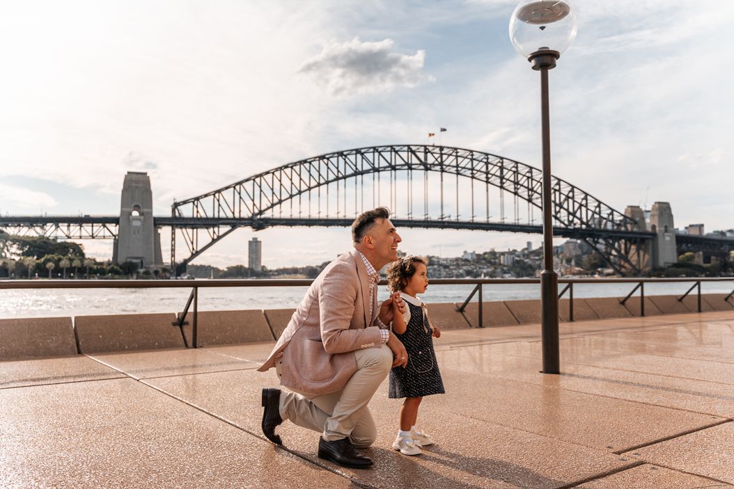 A daughter and her dad gazing at a bird during a family photoshoot in Sydney, with the Harbour Bridge beautifully framed