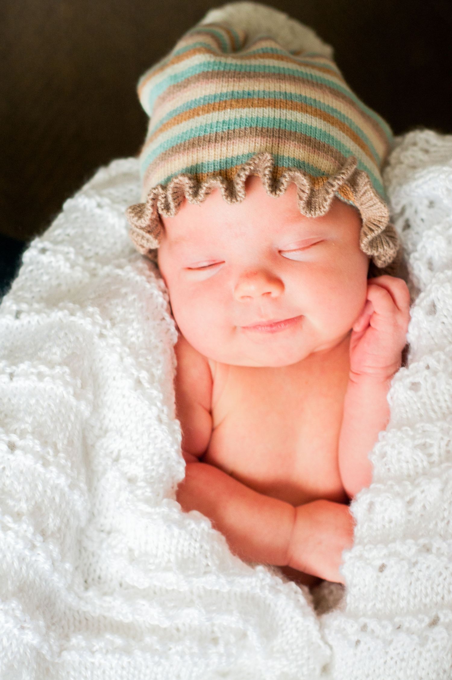 A sleeping newborn baby wrapped in white blankets wearing a striped knit hat.