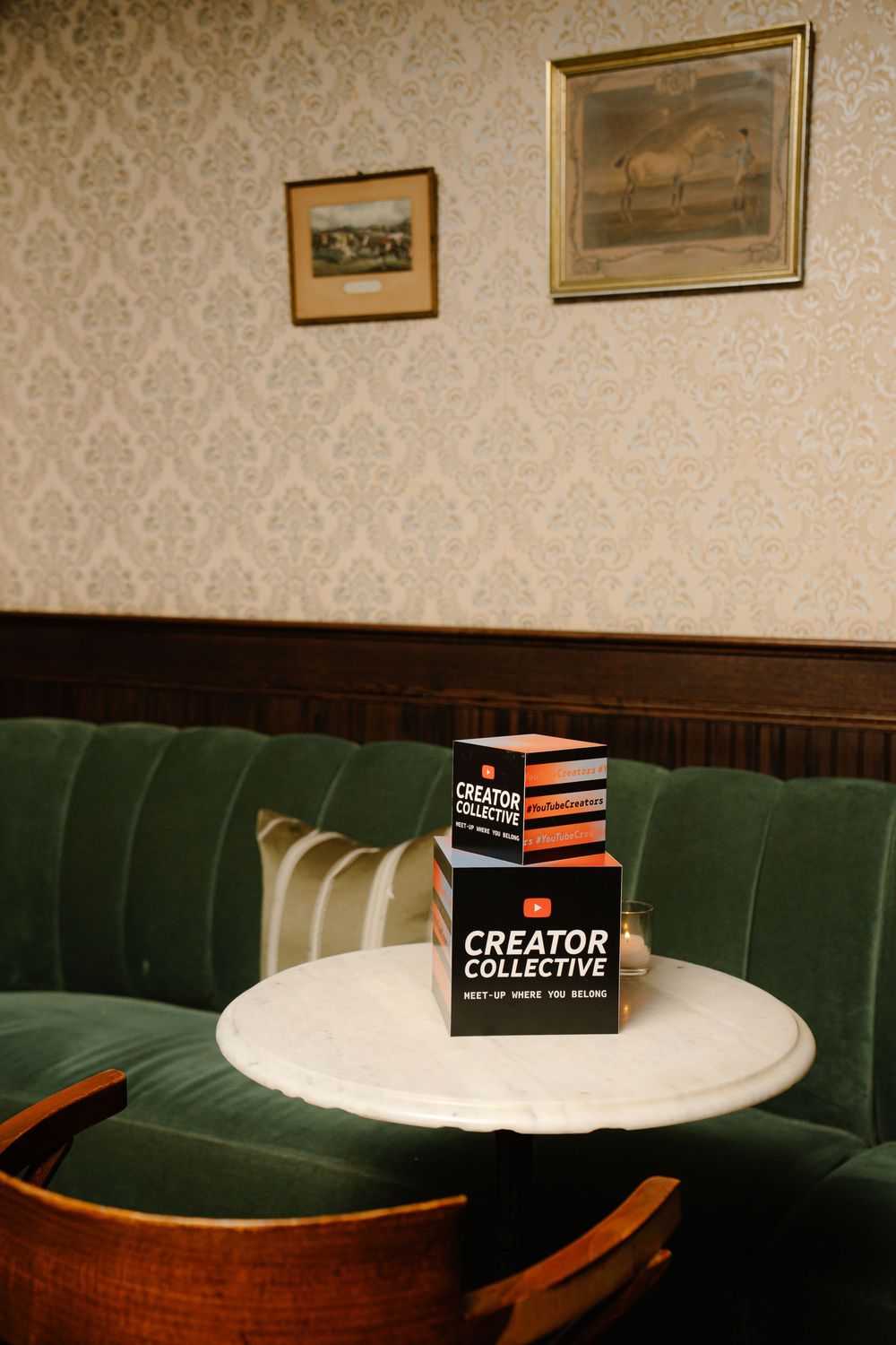 Black Creator Collective card box sits on white marble table against green vintage booth seating and patterned wallpaper.