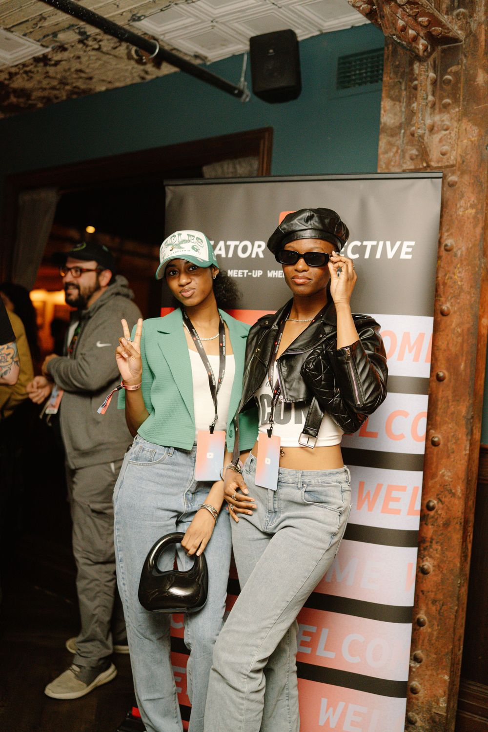 Two people pose in casual outfits with denim jeans at an indoor event with a branded backdrop display.