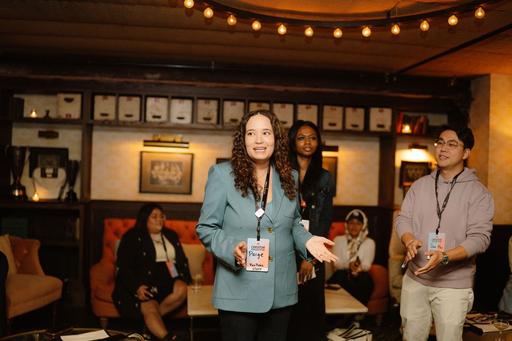 A professional speaker engages with the audience in a dimly lit venue decorated with string lights and framed artwork.