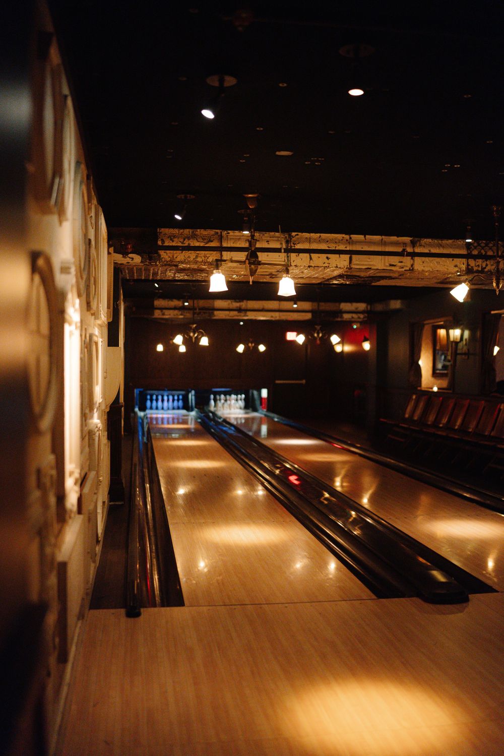 Vintage bowling alley lit with warm ambient lighting and pendant lamps illuminating polished wooden lanes.