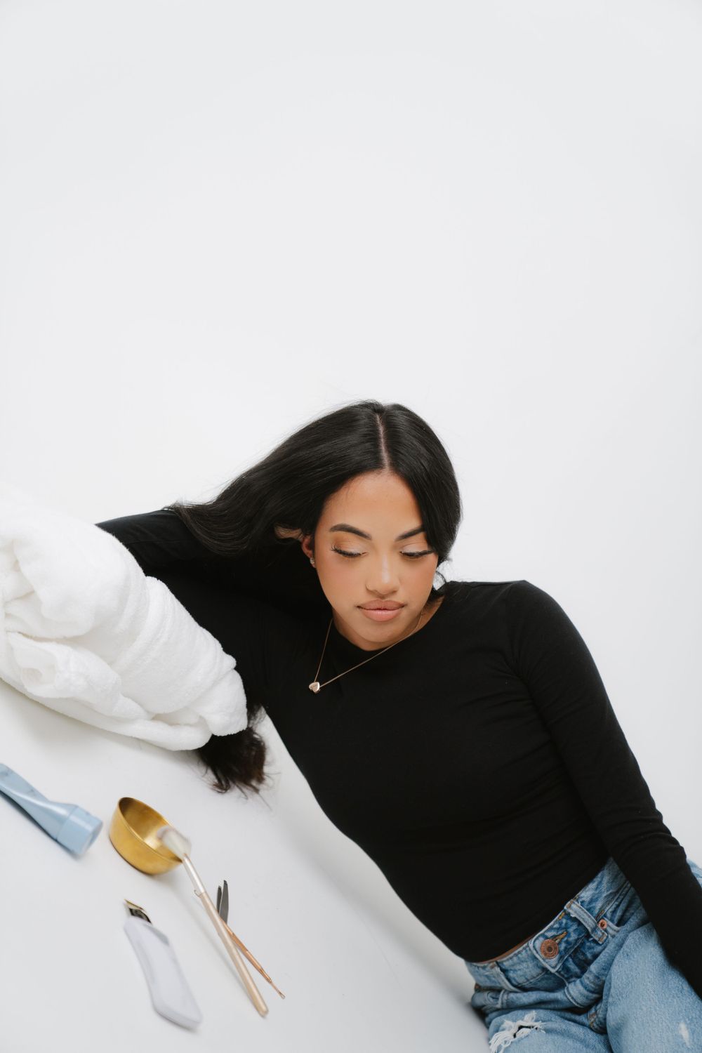Someone in a black turtleneck and jeans lies on a white surface next to cutlery and kitchenware.