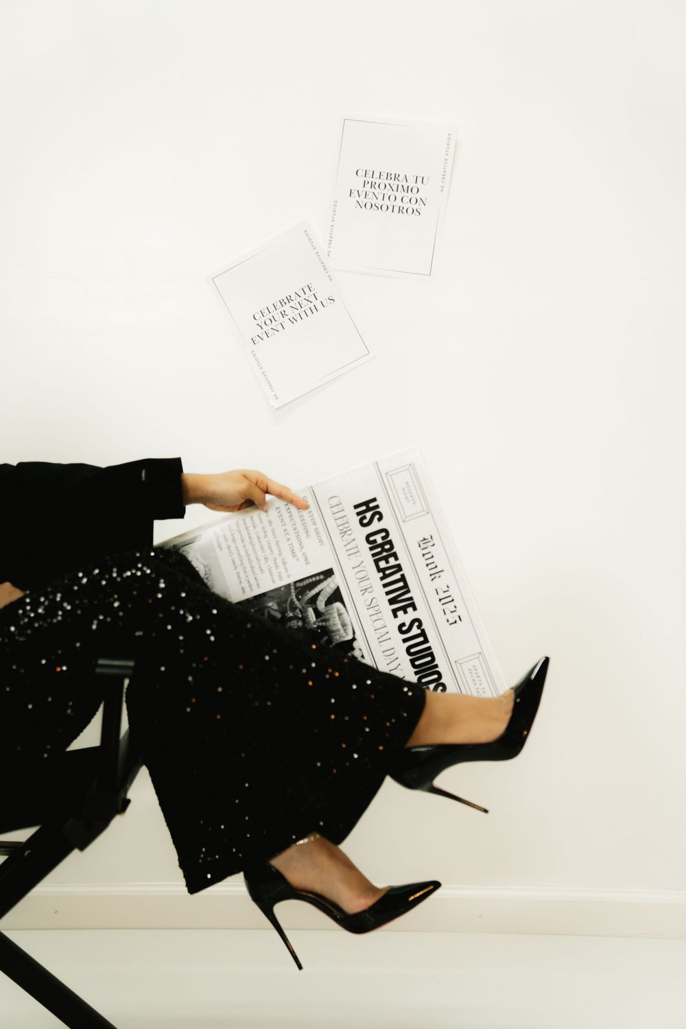 Stylish legs in black pants and heels with scattered papers in a minimalist editorial setting.