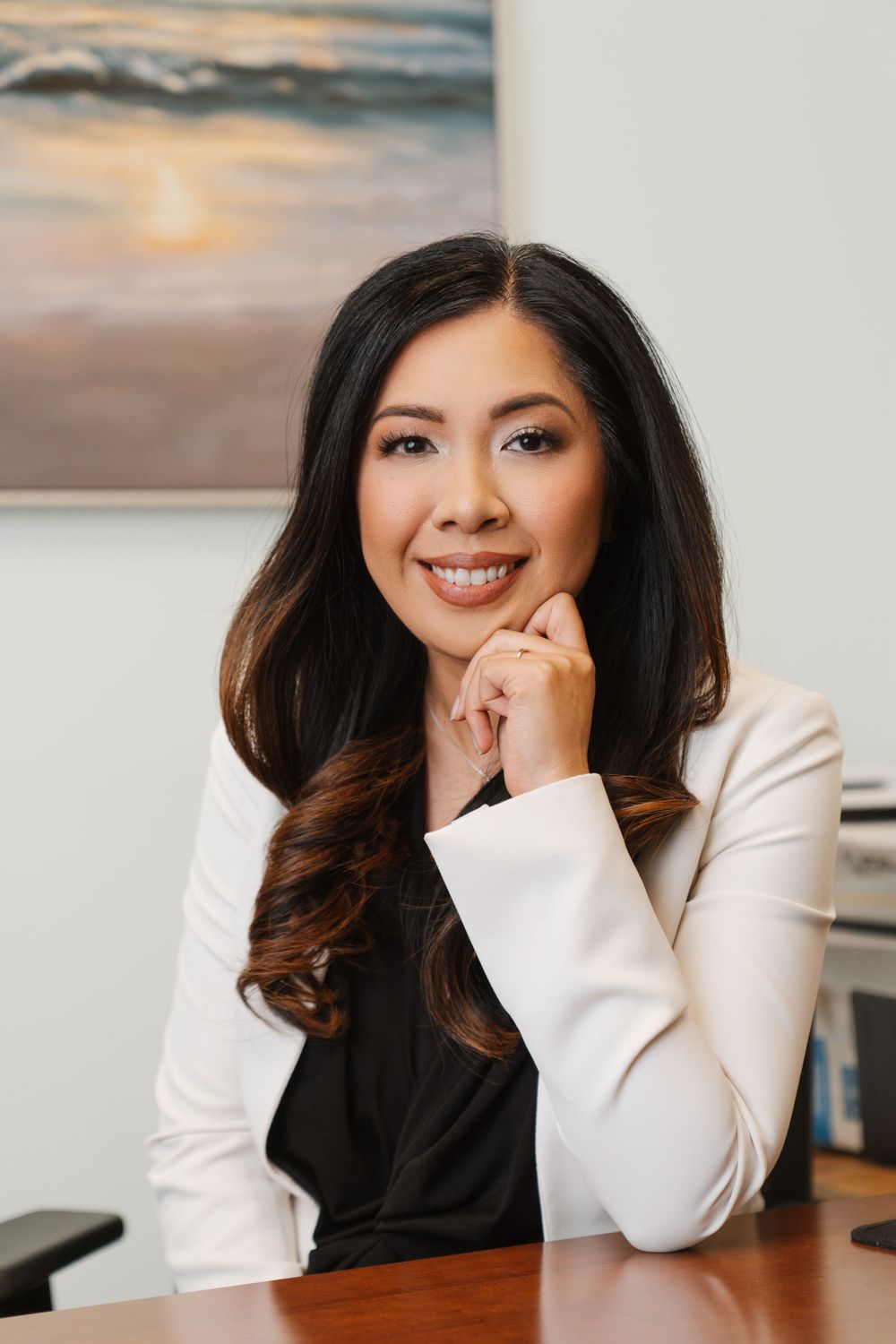 Professional headshot of someone in a white blazer smiling warmly against an office backdrop.