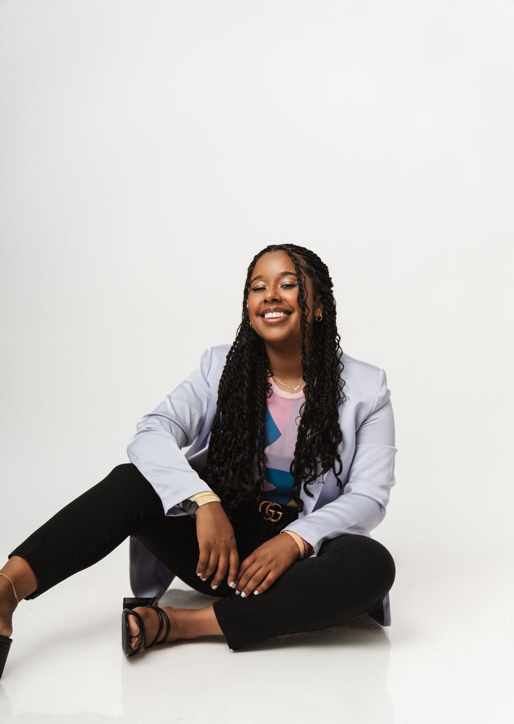 Casual studio portrait of someone in a light blue jacket and pink top sitting cross-legged.