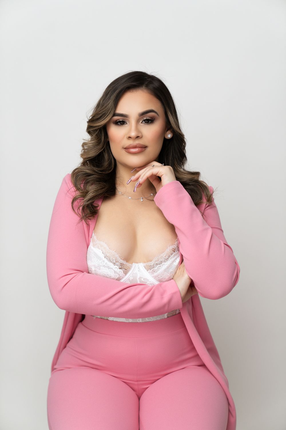 Fashion portrait in pink matching outfit with white lace detail against white background.