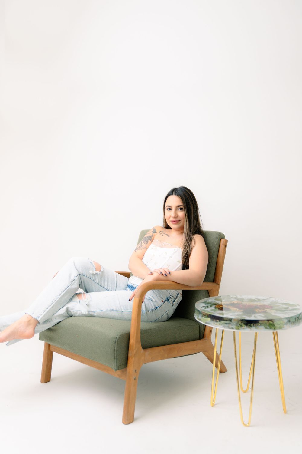 Someone relaxes in a mid-century modern green armchair next to a marble side table against a white backdrop.