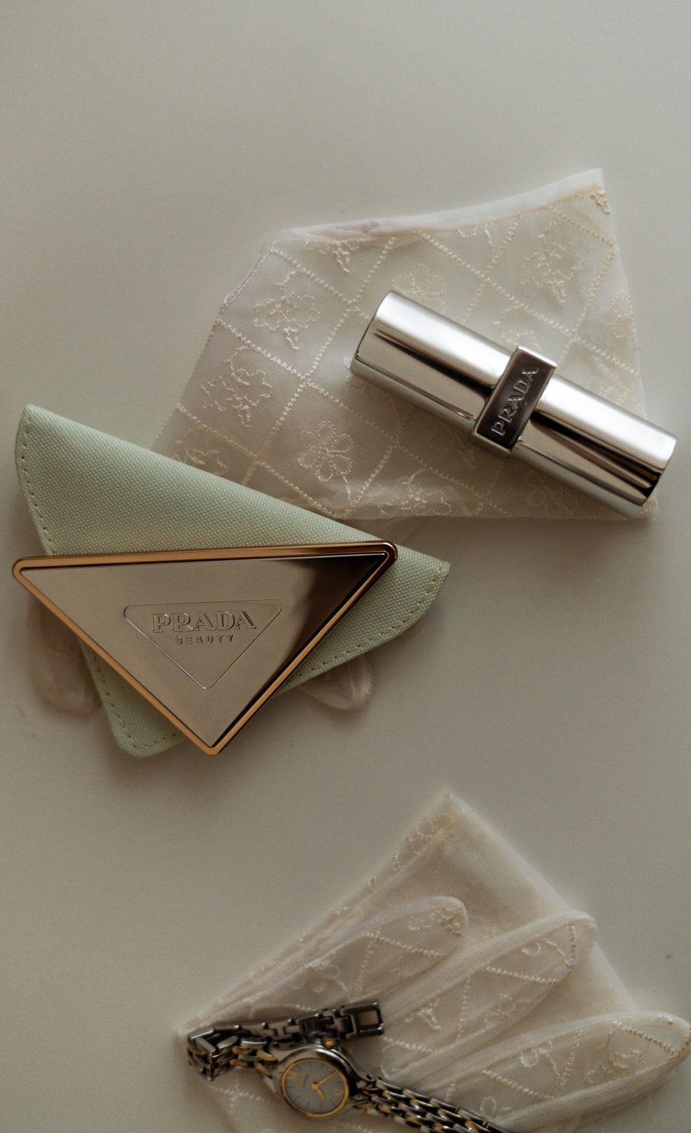 A Prada mint green wallet with silver embellishments and a watch on a neutral surface.