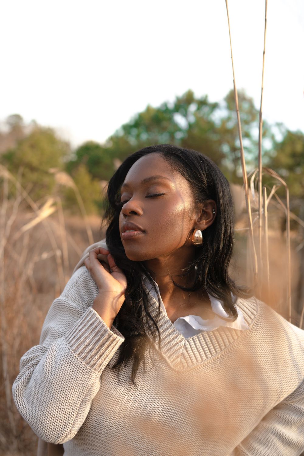 Portrait in warm sunlight of someone wearing a beige knit sweater in a field of tall dry grass at golden hour.