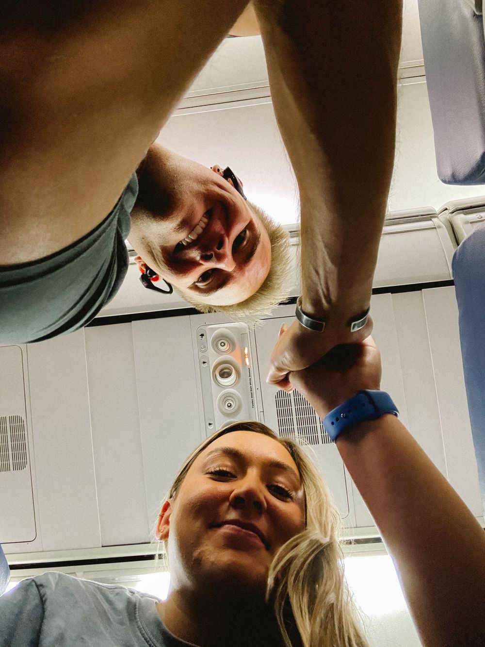 Two people taking a fun upside-down selfie perspective photo inside an airplane cabin.