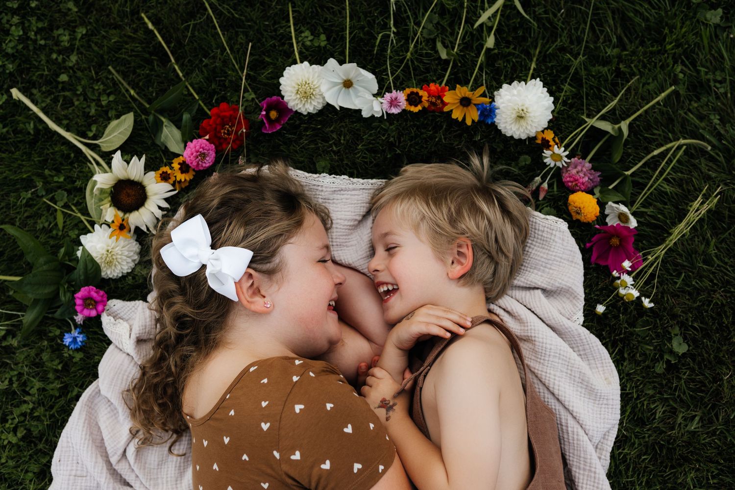 Two people lying on blanket under floral arch made of colorful blooms.