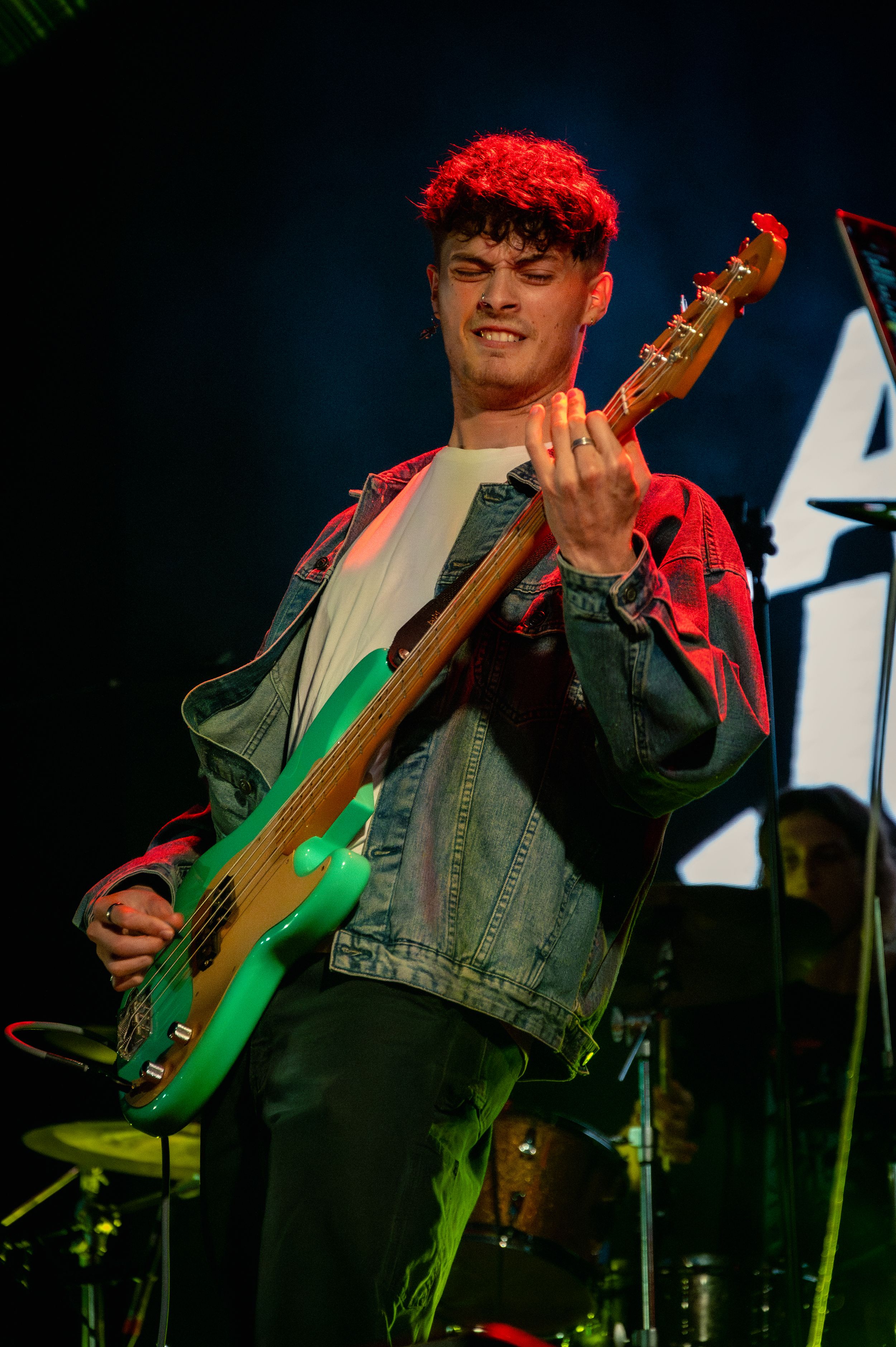 Bass player with dyed red hair performing under dramatic stage lighting.