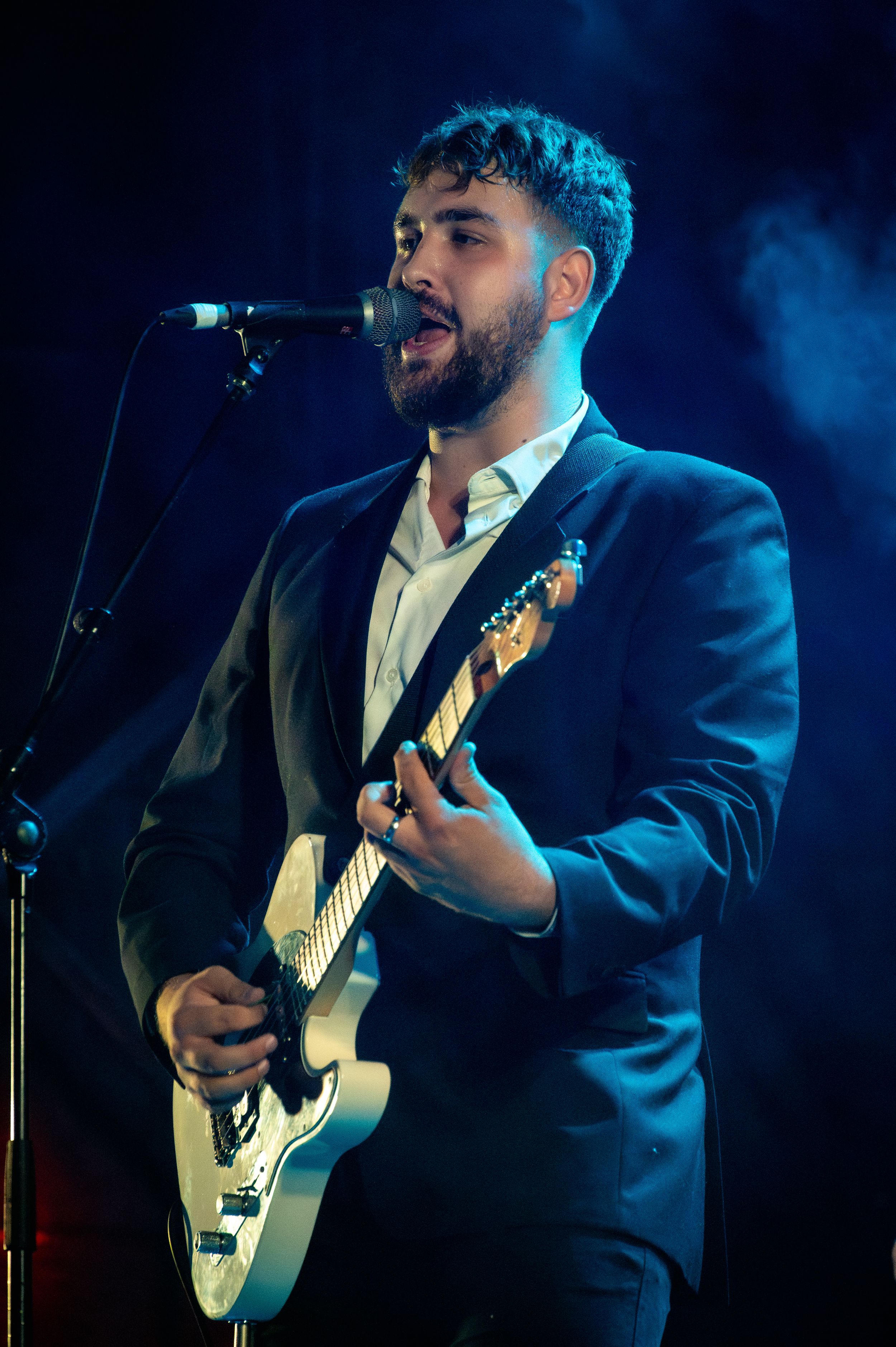 Singer-guitarist performing passionately in a suit under blue stage lighting.
