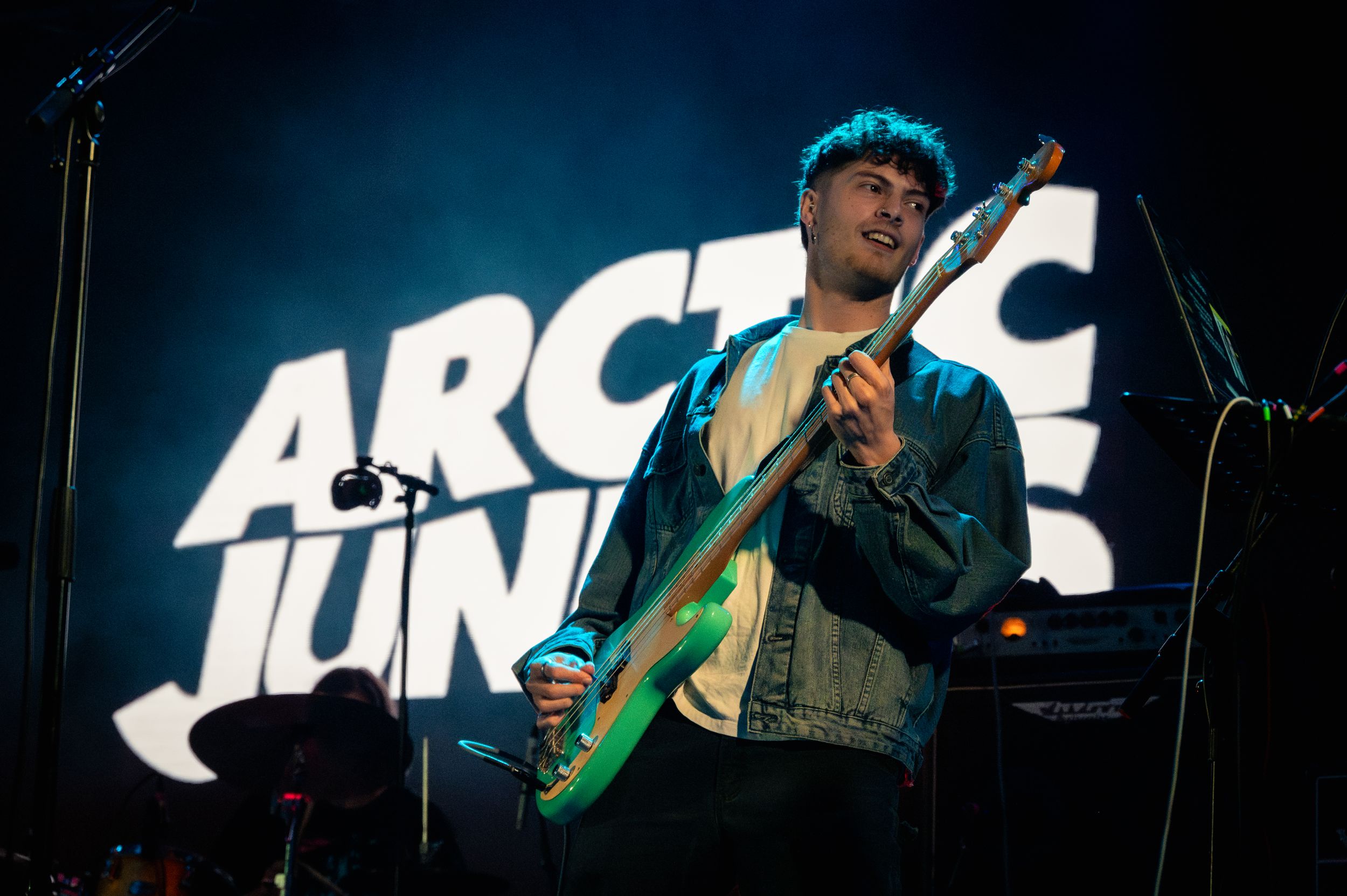 Musician playing bass guitar during Arctic Junks concert with dramatic blue stage lighting.