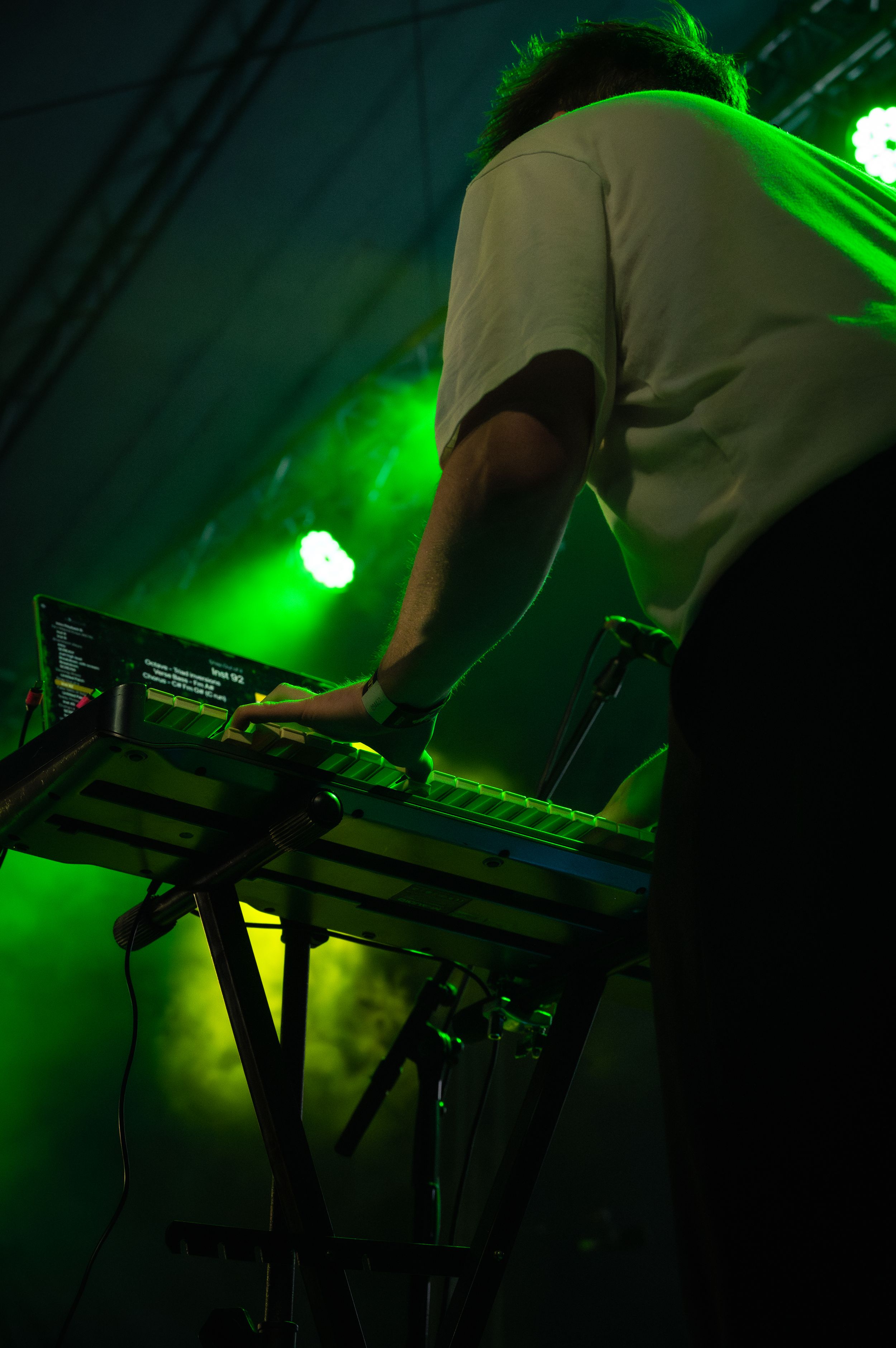 Musician operating keyboard equipment under dramatic green stage lighting at a live performance.