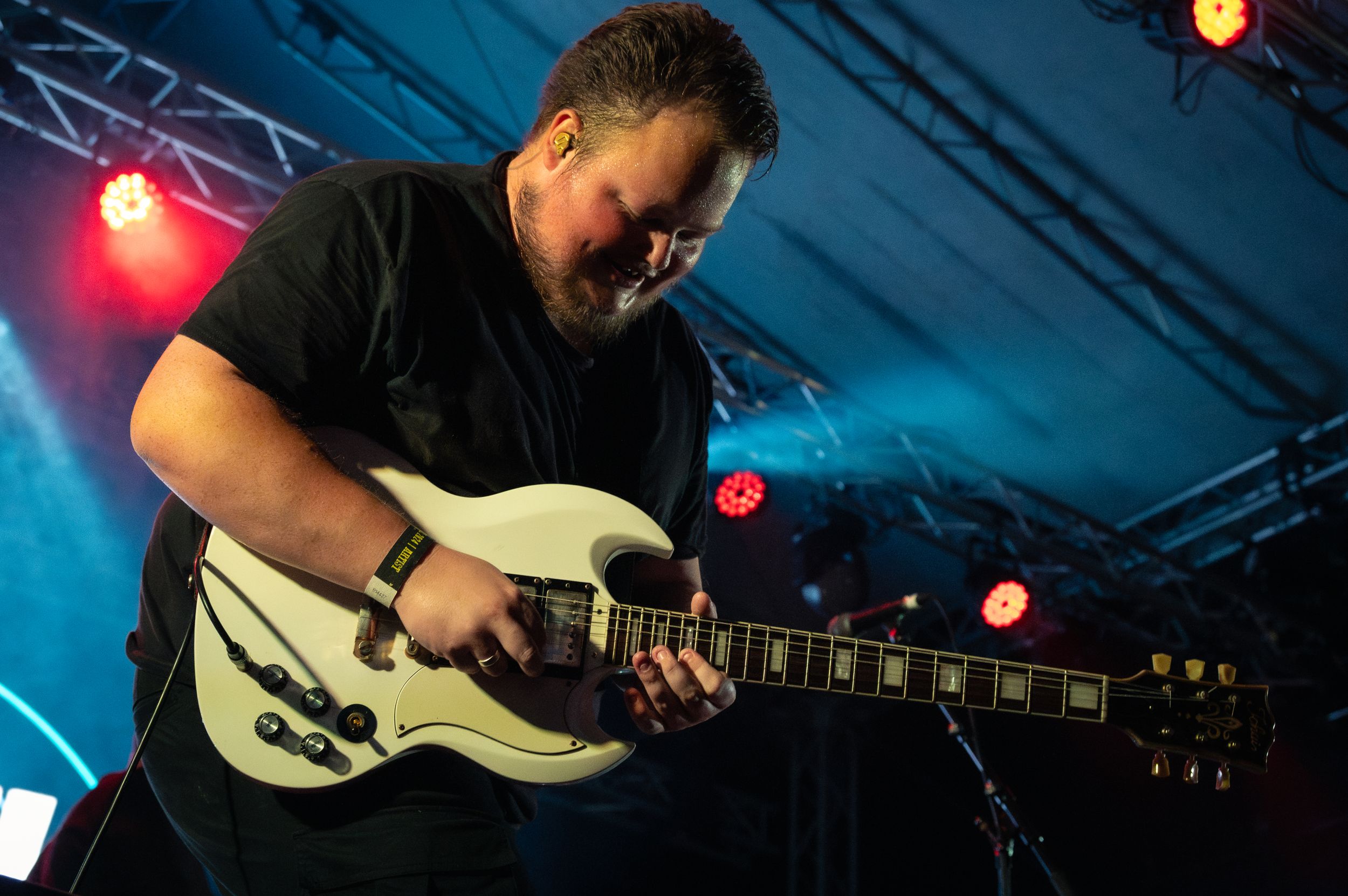 Guitarist playing white electric guitar under blue and red stage lights.
