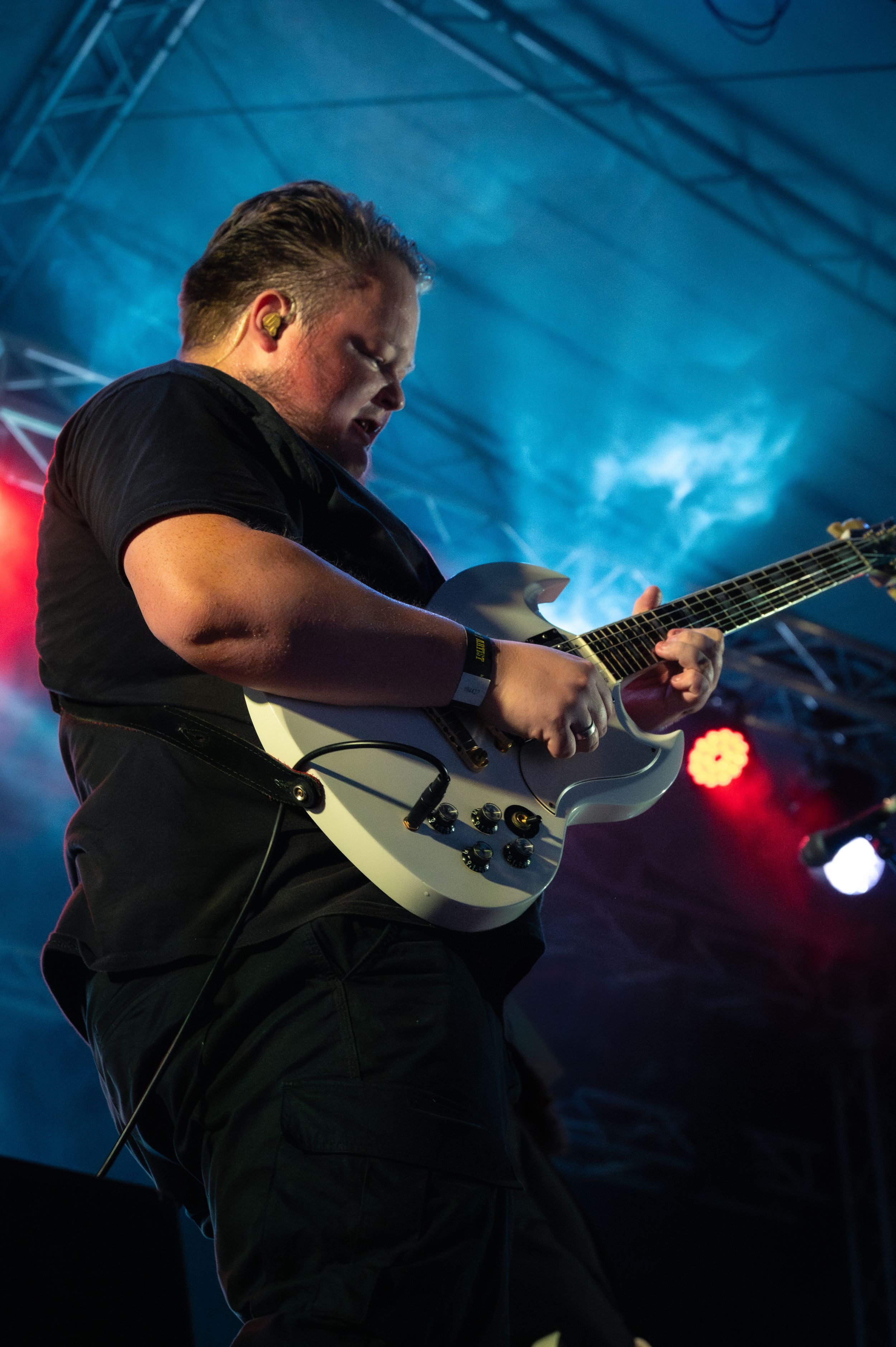 Musician playing white guitar on stage with dramatic blue lighting and fog effects.