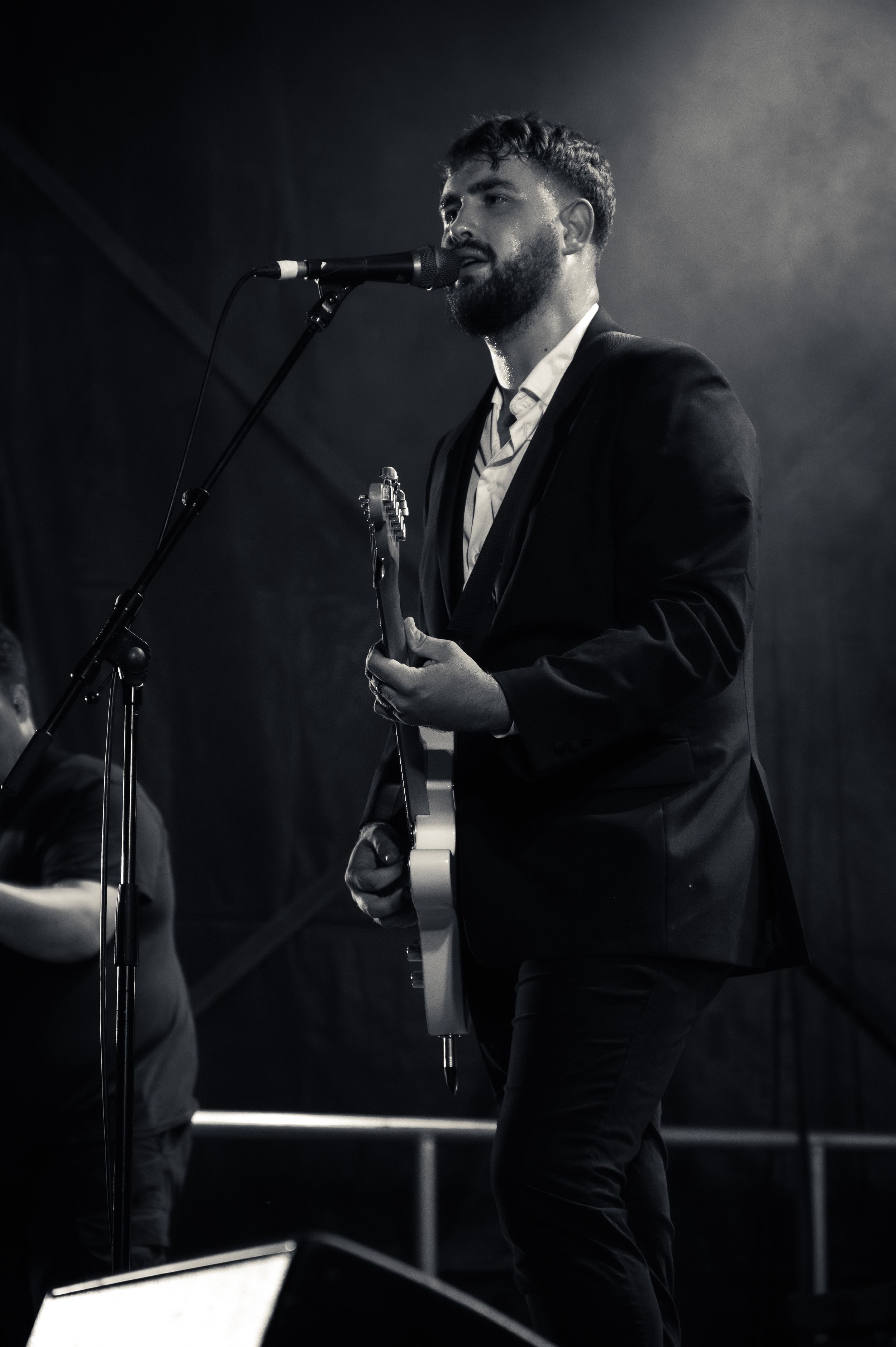 Performer in black suit singing into microphone on dimly lit stage.