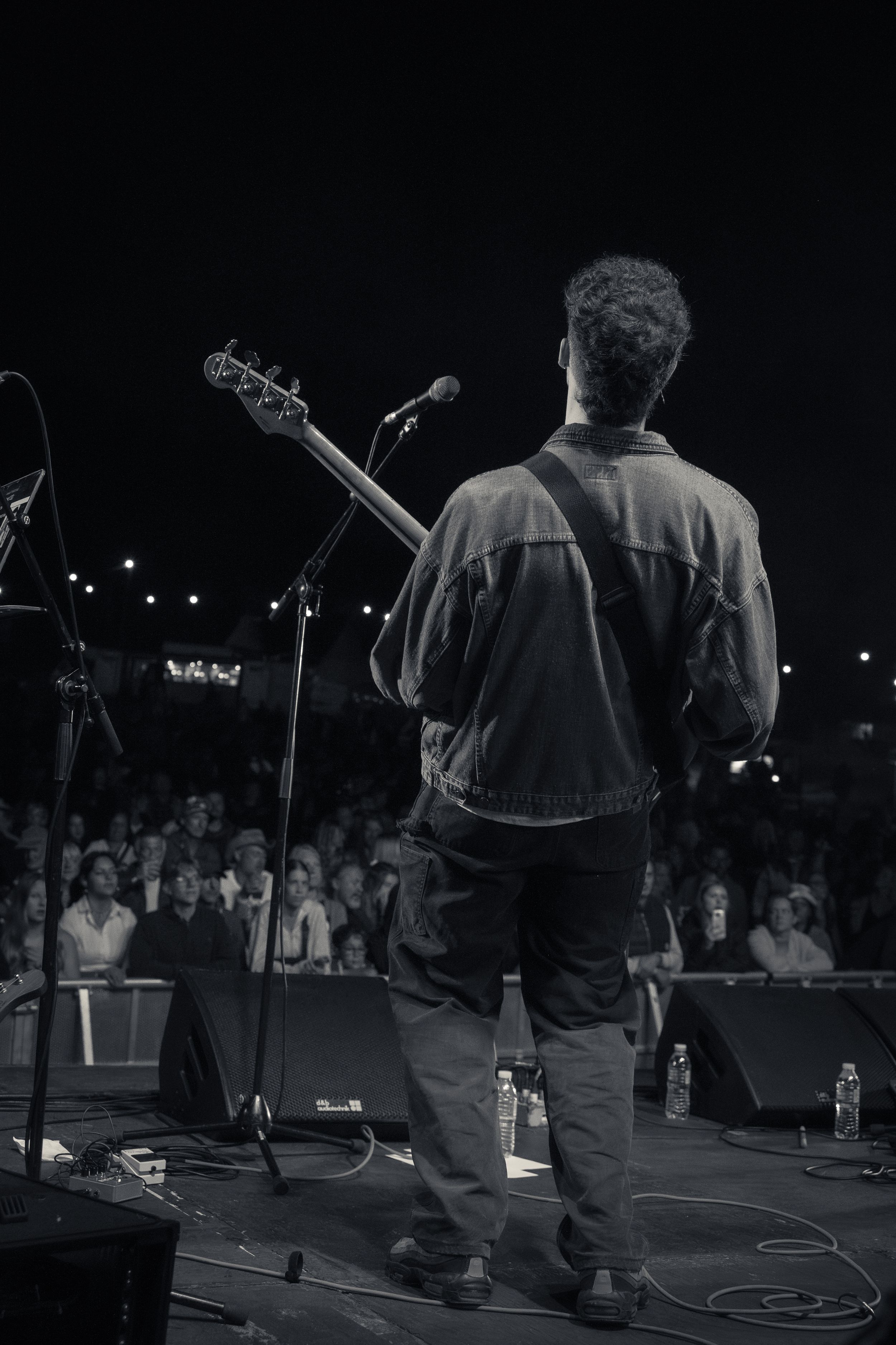 Silhouetted musician playing guitar on stage with crowd visible in background.