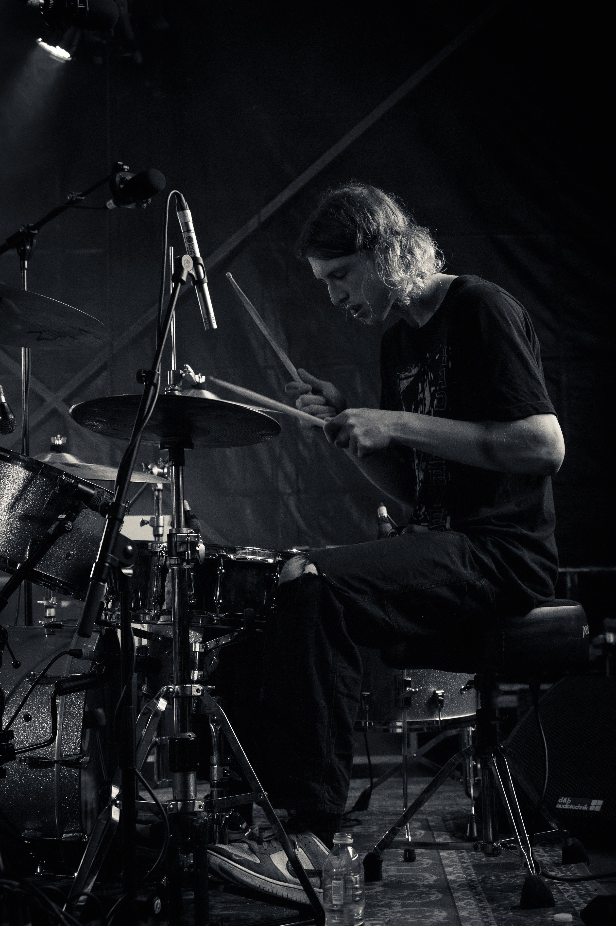 Drummer performing on dark stage with dramatic side lighting and drum kit setup.