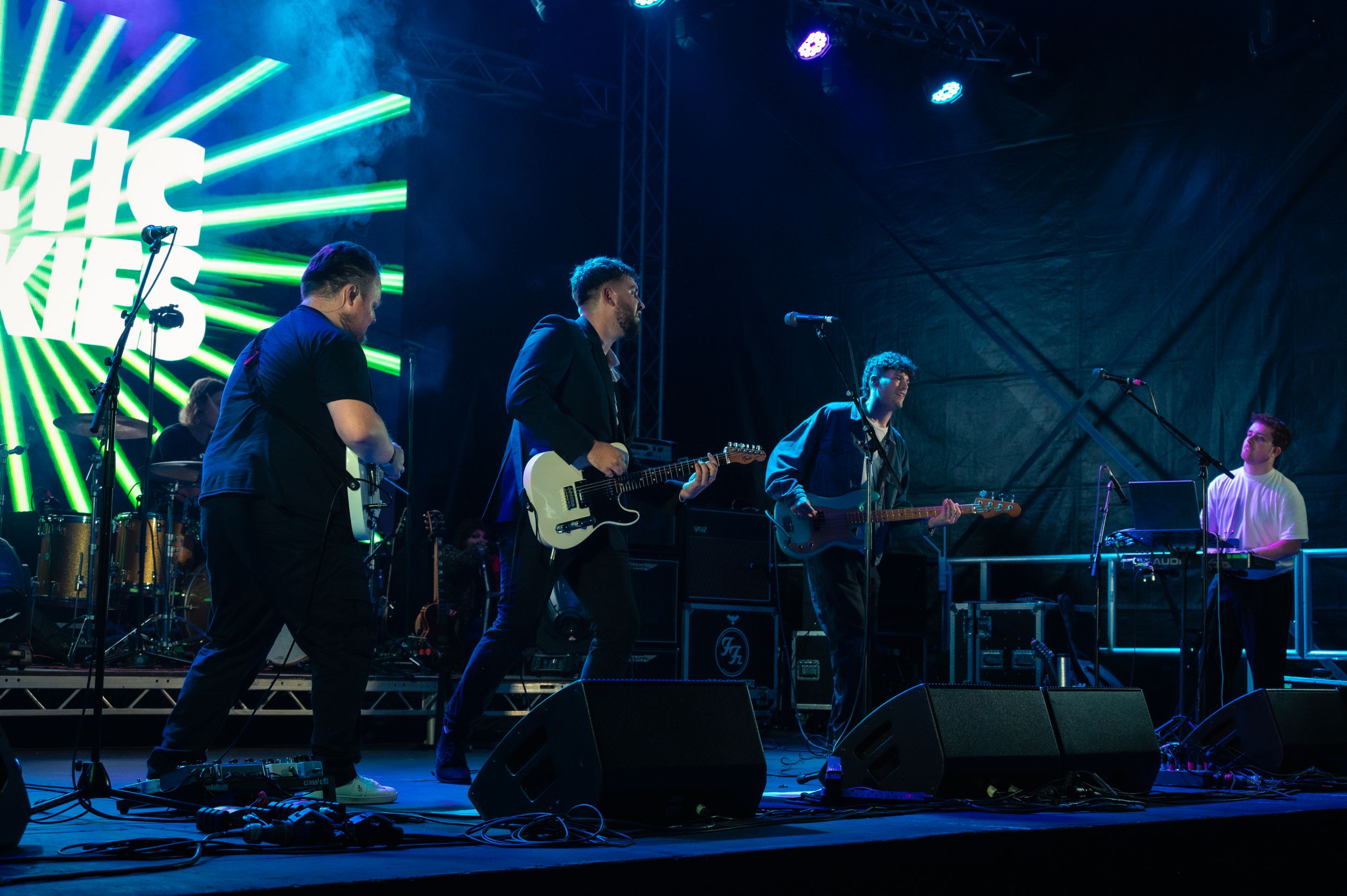 Rock band performs on stage with bright neon lights and musical equipment during a live concert.