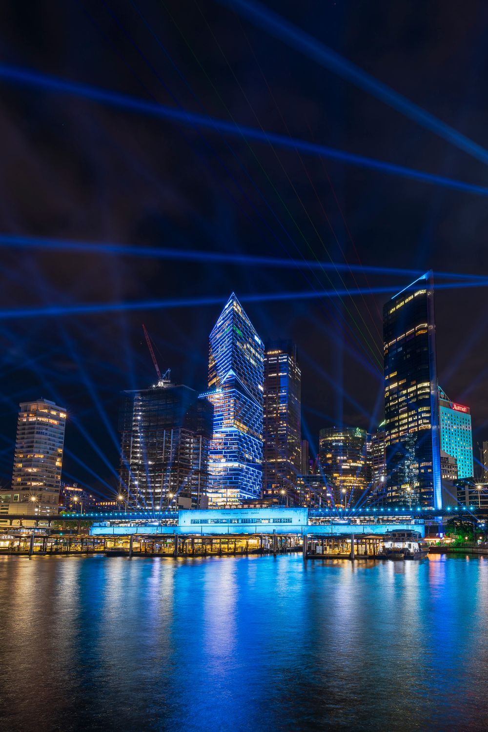Brisbane city skyline at night with blue laser light show reflecting on the river during Vivid festival.