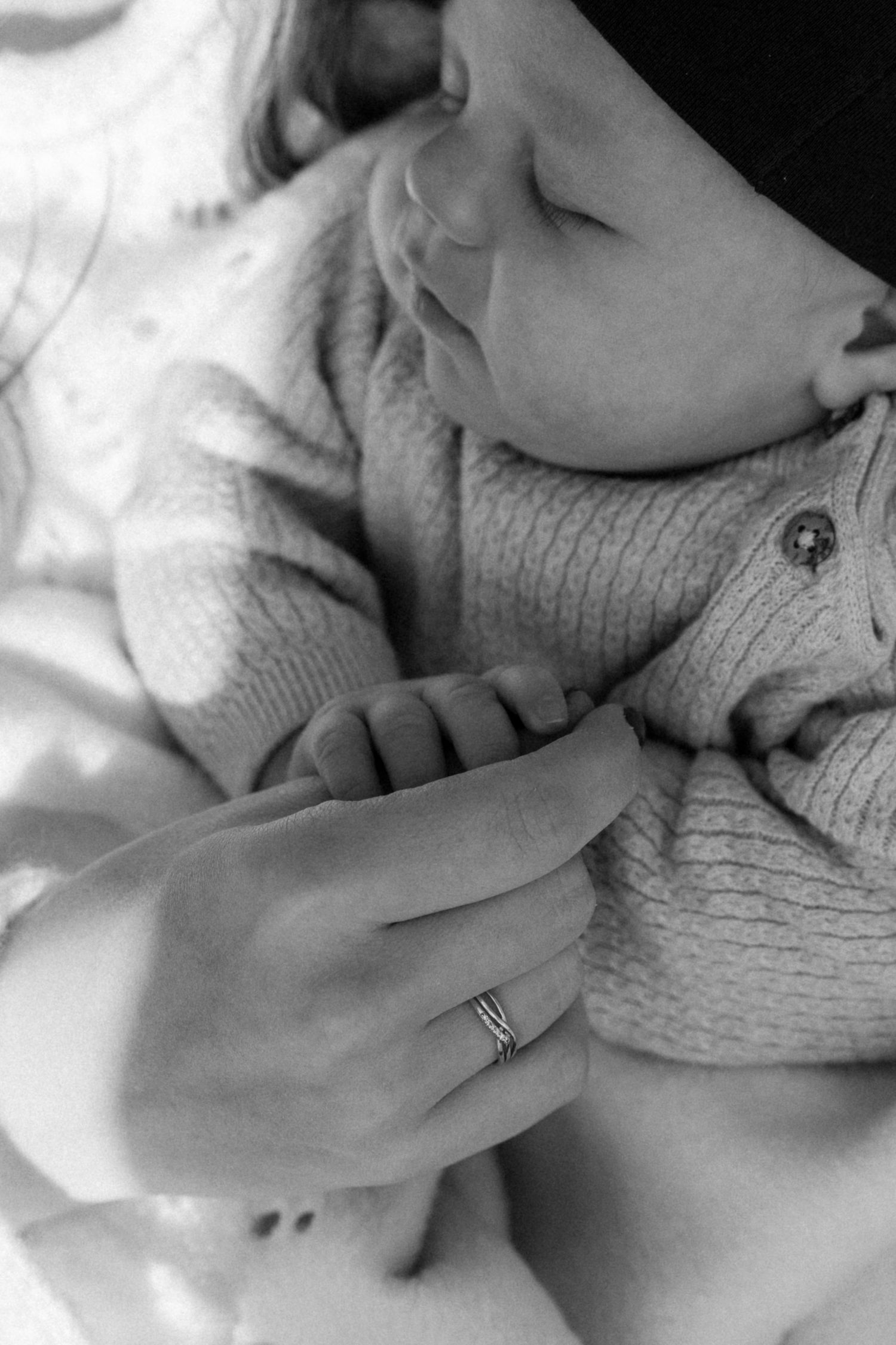 Close-up black and white photo of sleeping baby in knit sweater with hand detail.