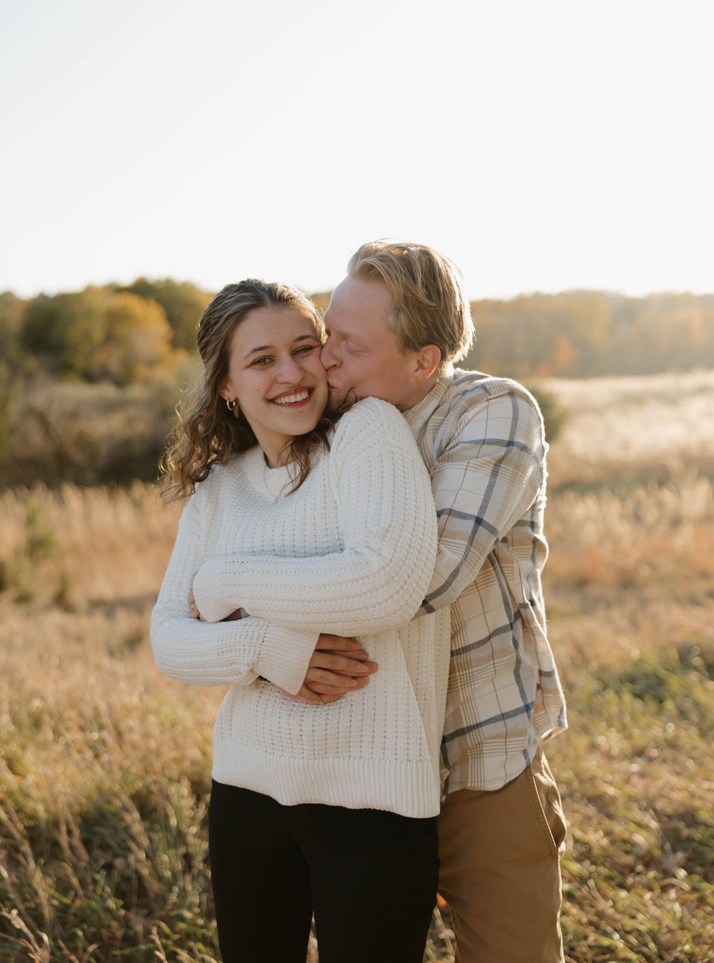 A couple in autumn attire sharing tender moments in a golden sunlit field at sunset.