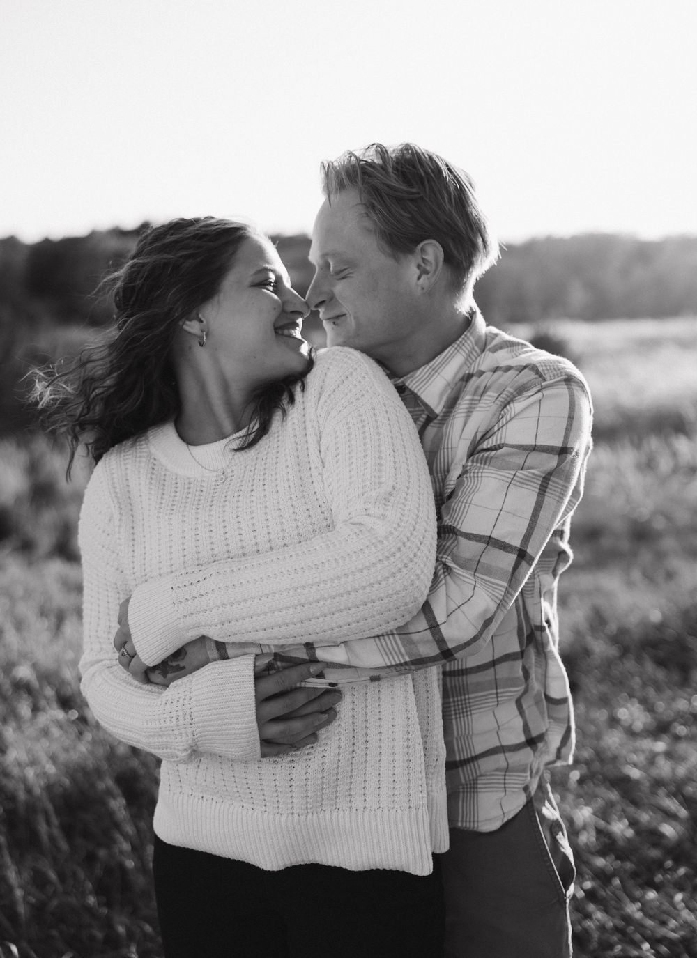 Black and white romantic photos of a couple embracing in a field during sunset, shown in multiple angles.