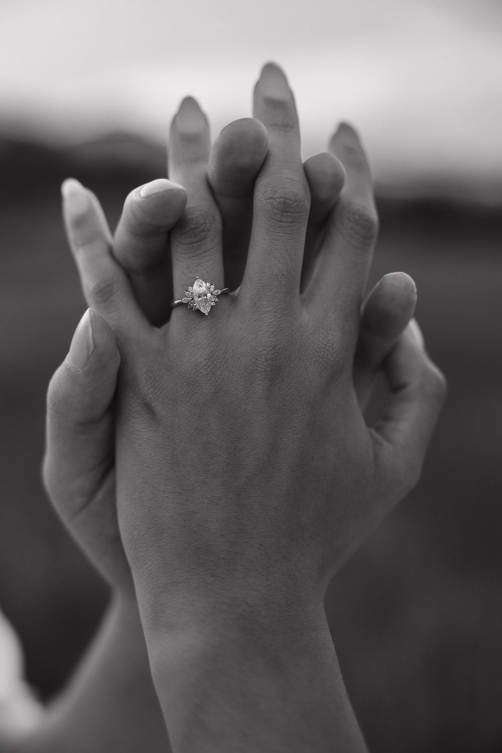 Close-up of hands clasped together with an engagement ring sparkling in black and white.