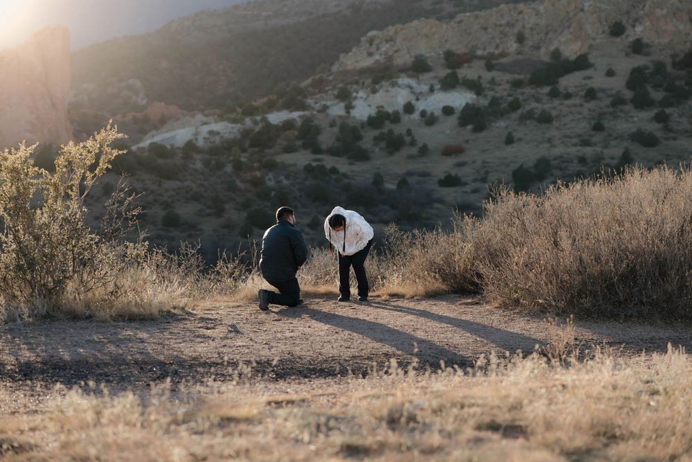 A sequence of people hiking and walking along a rugged desert trail during golden hour lighting.