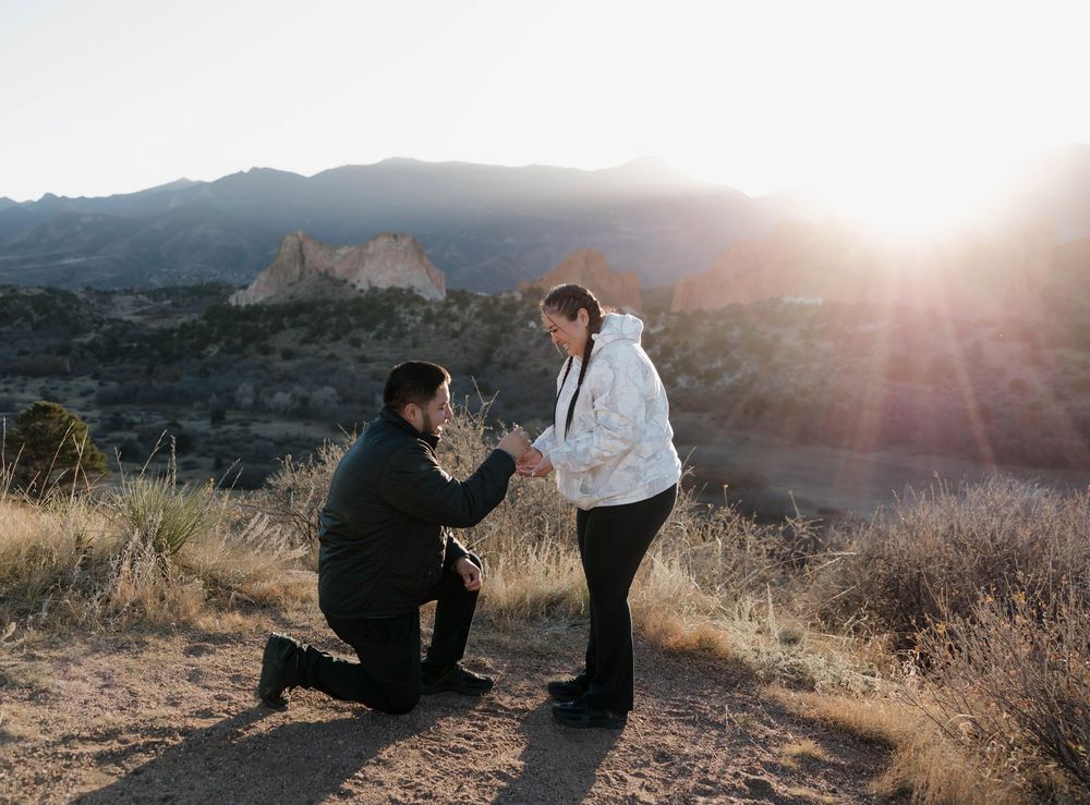 Silhouettes of a couple during a romantic sunset proposal on a mountain overlook with lens flare.