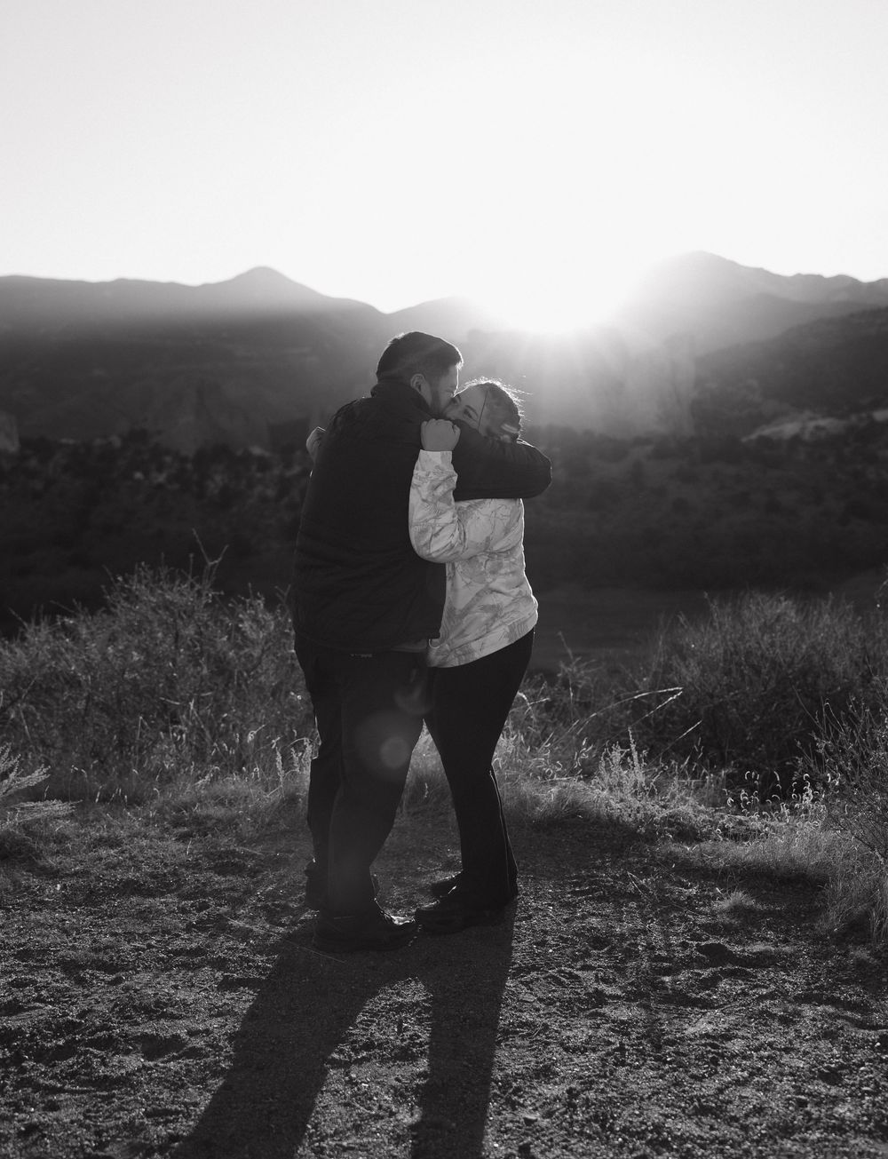 Two silhouetted figures dance together against a misty mountain landscape at sunset in black and white.