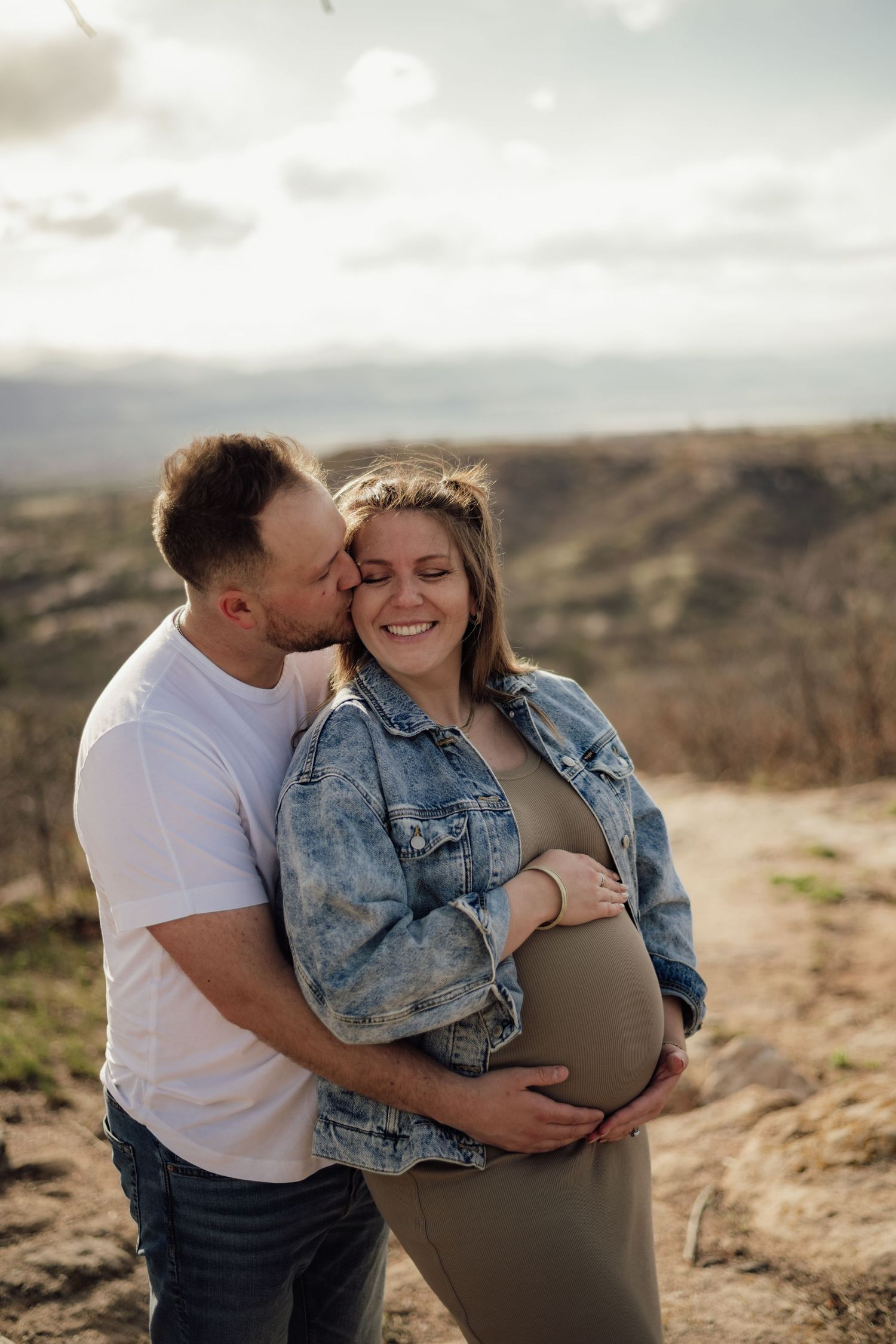 Couple sharing tender moment on desert hillside during maternity photoshoot.