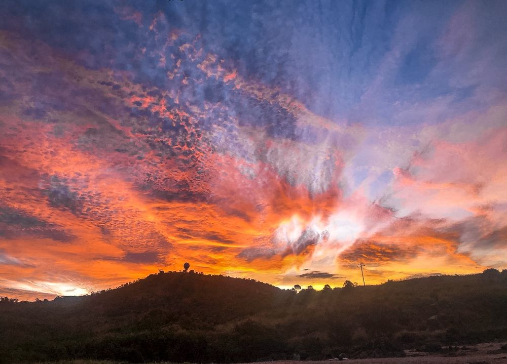 Dramatic sunset sky with vibrant orange clouds and sunrays over silhouetted mountain landscape.