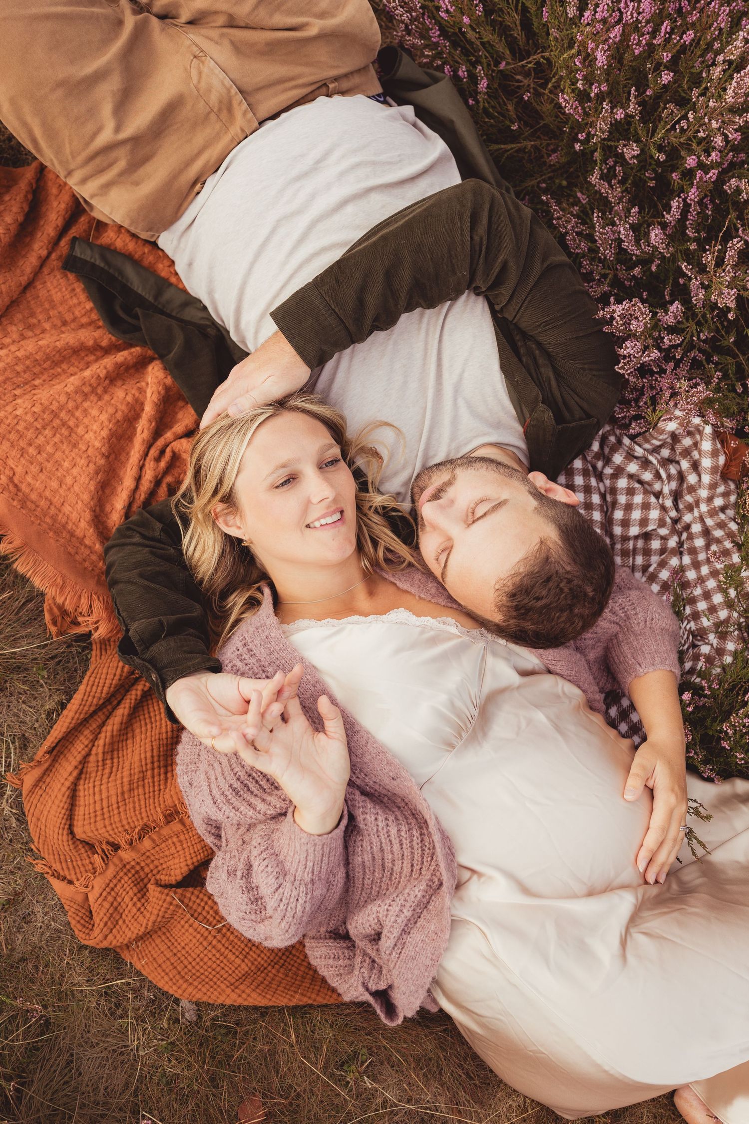 Couple lying on a blanket outdoors near heather flowers, smiling and relaxing together in autumn.