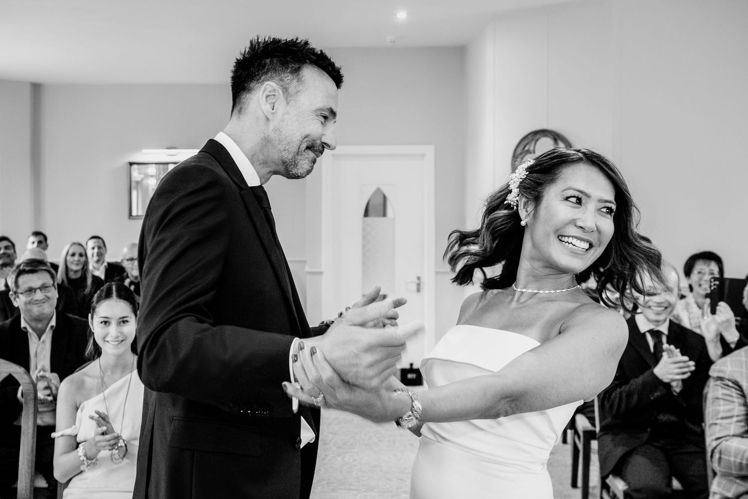Black and white photo of a joyful bride and groom exchanging rings at their wedding ceremony.