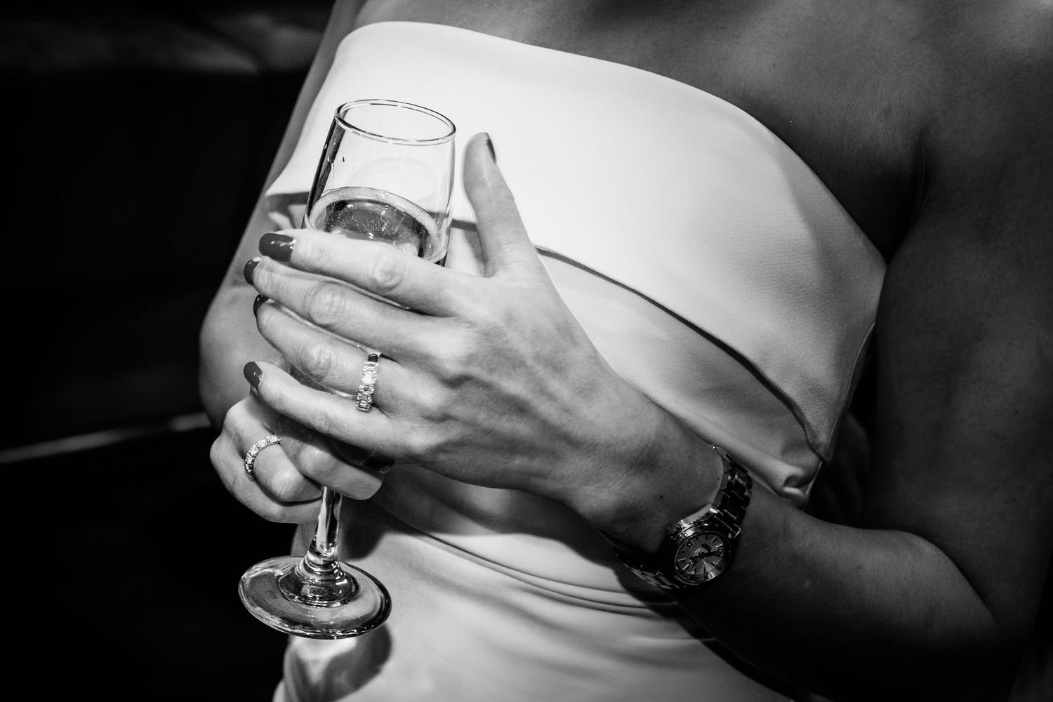 Close-up of a bride holding a champagne glass, wearing a strapless white dress and a watch.