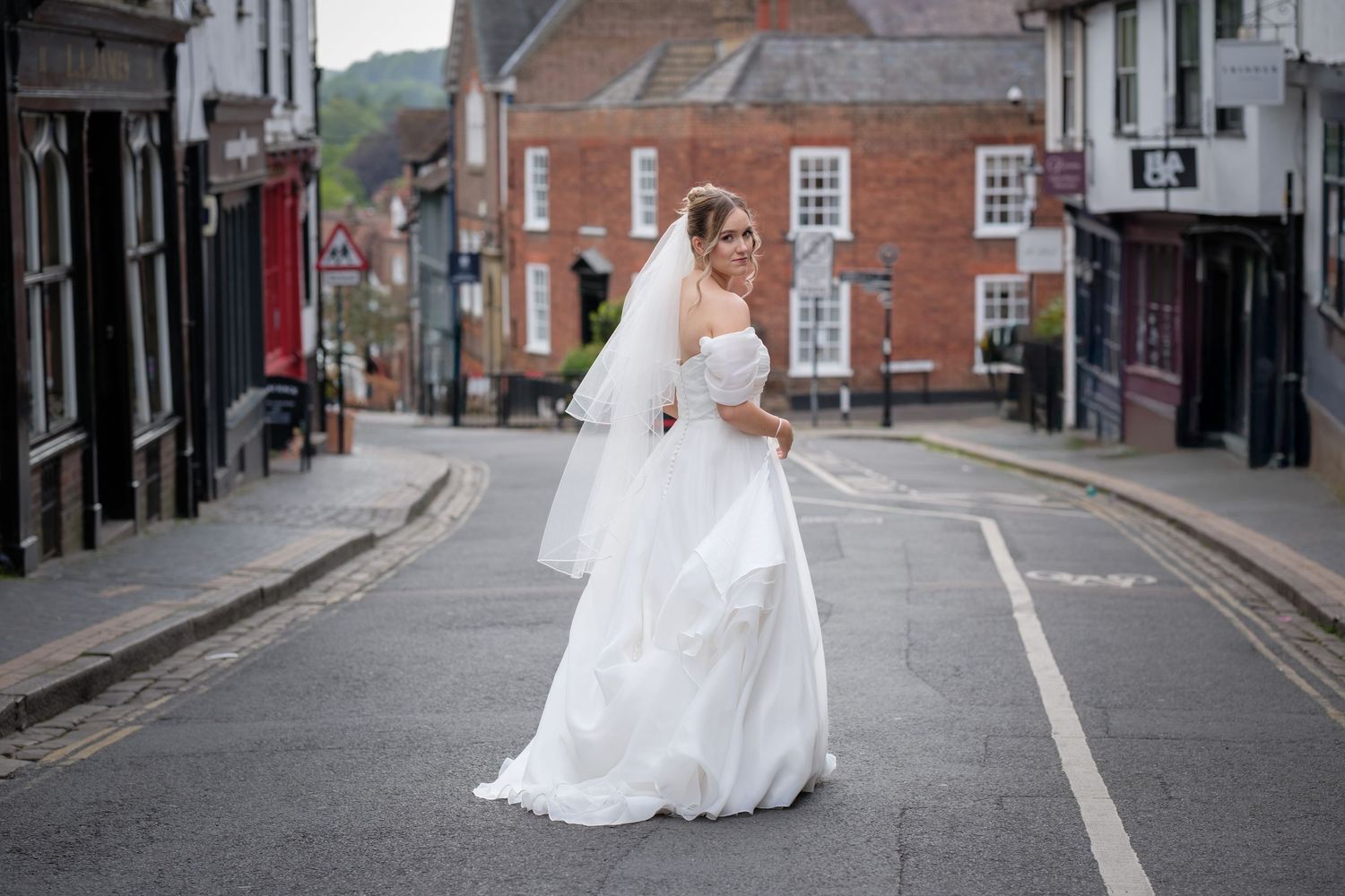 Bride in a white wedding gown and veil posing gracefully in the middle of a quiet town street.